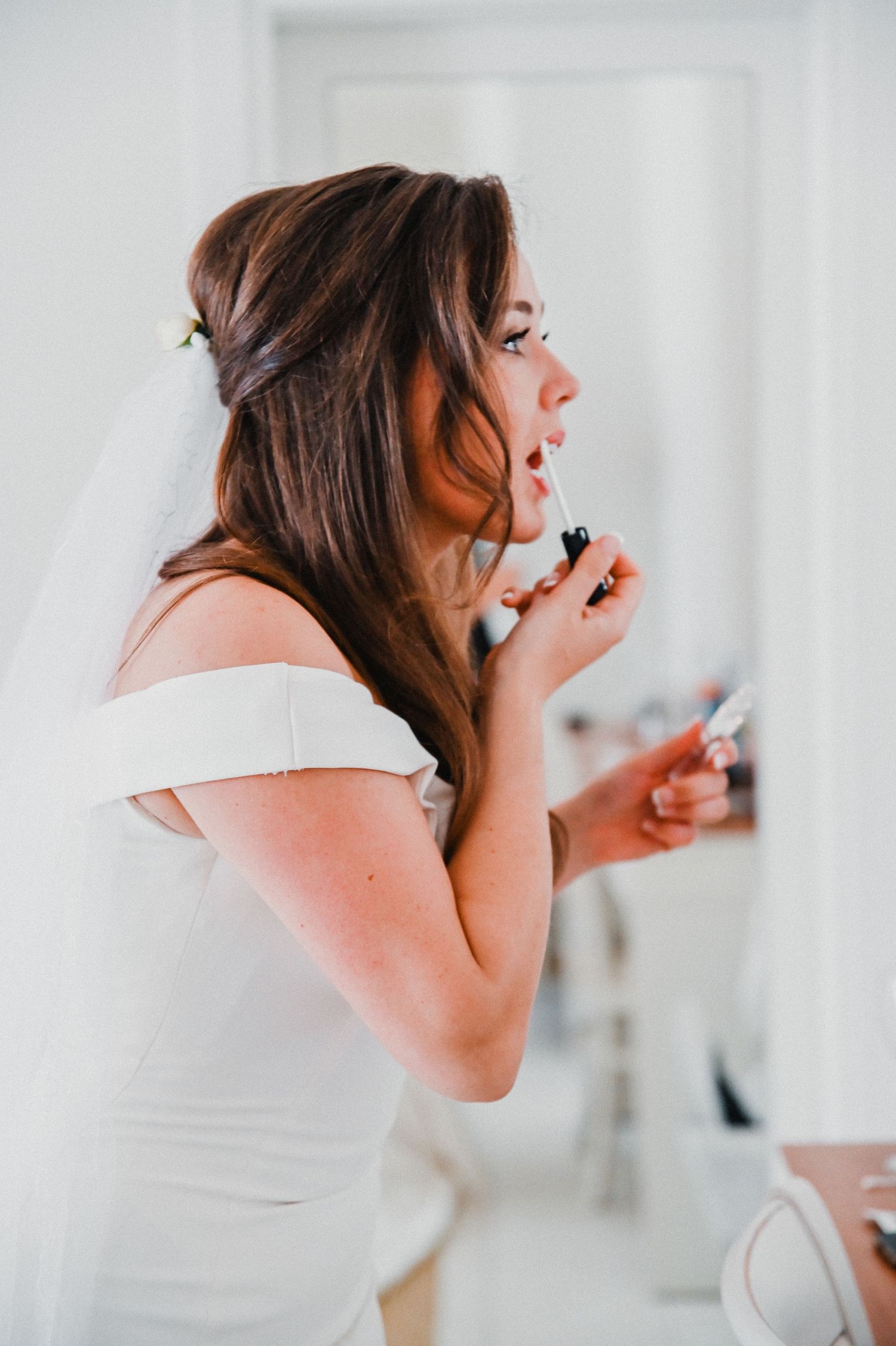A bride in white getting ready for her wedding day while applying makeup.