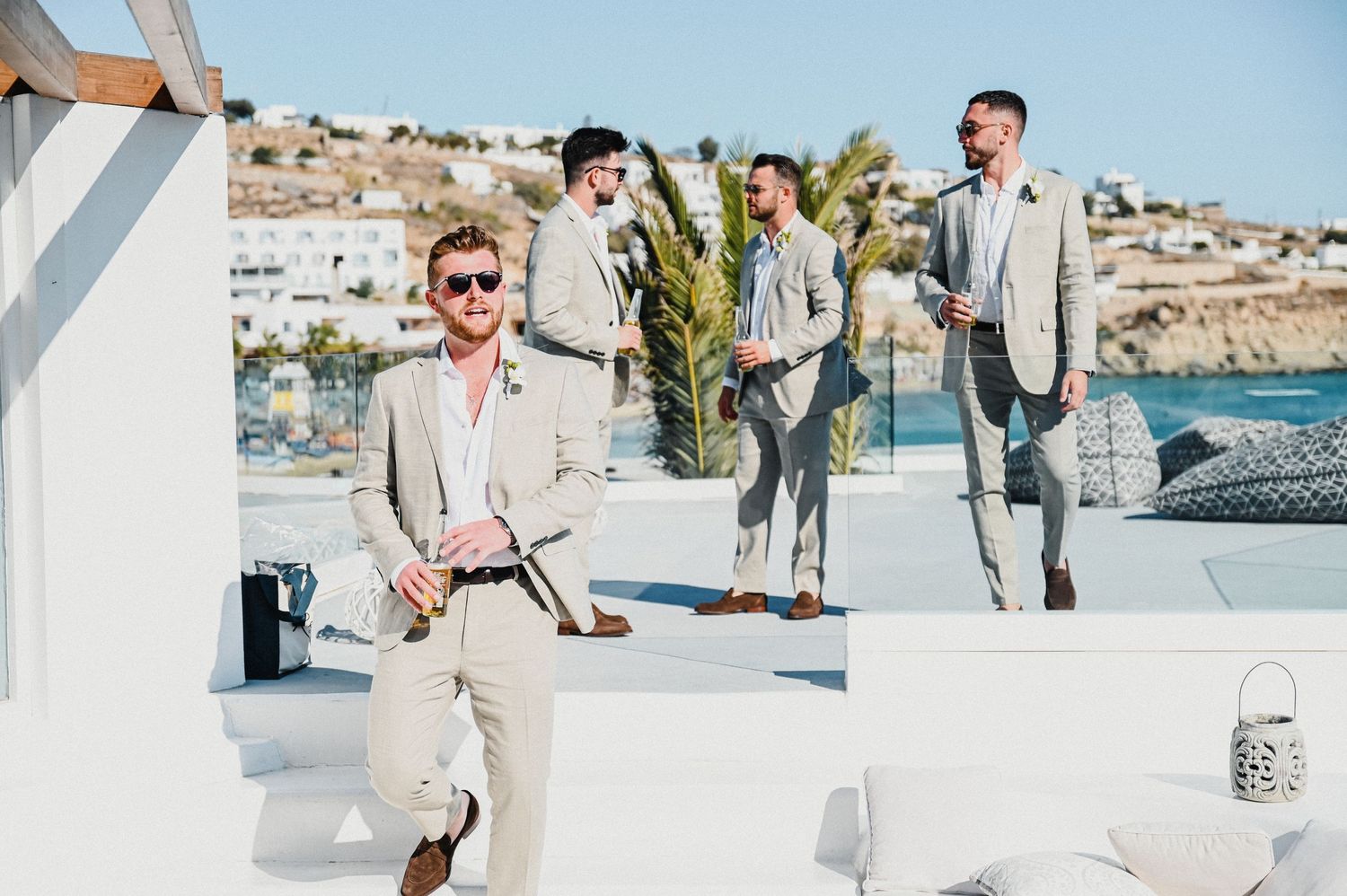 Bridal party relaxes on white Mediterranean terrace with coastal views in background.