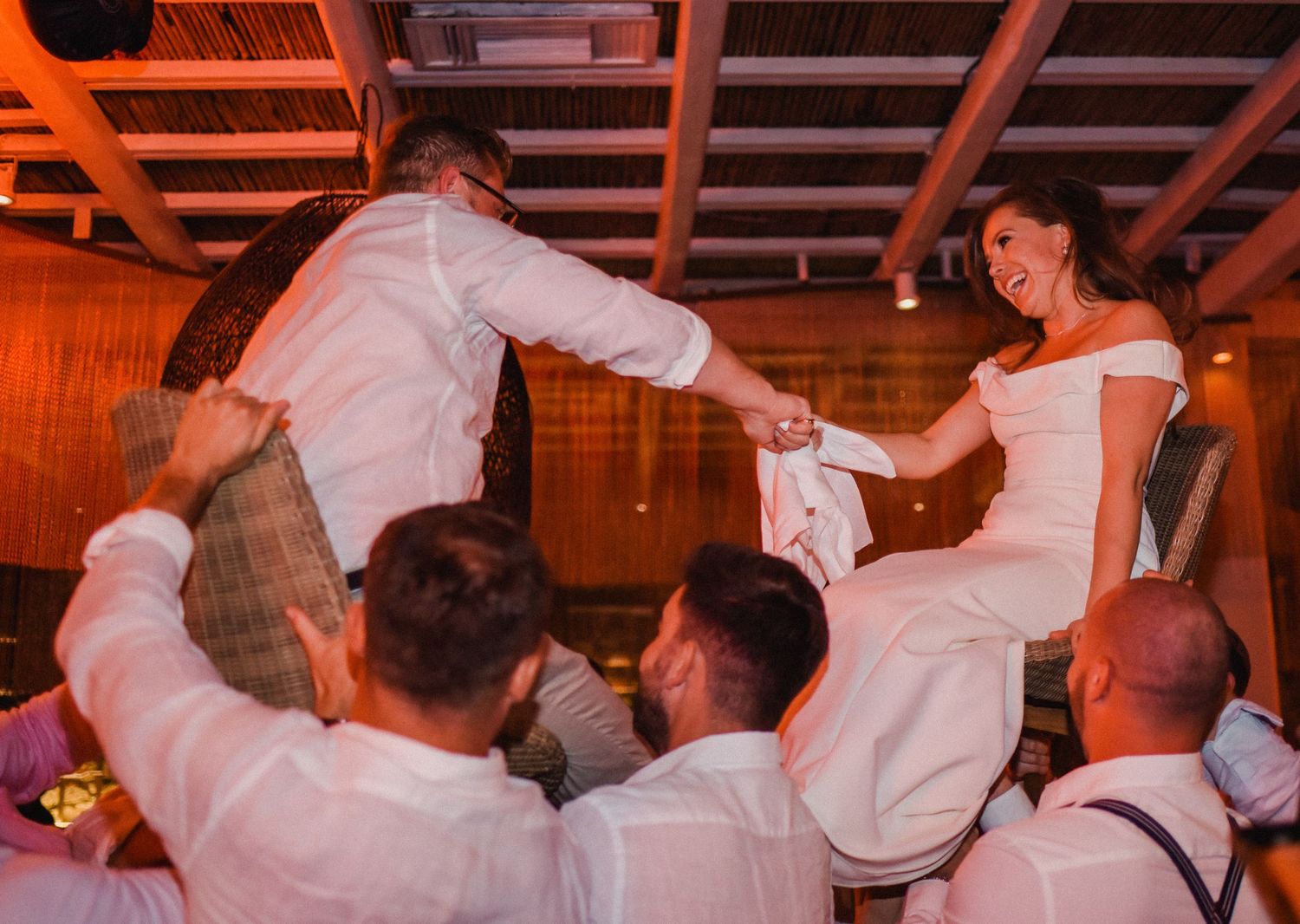 Wedding party lifts couple on chairs during traditional hora dance at reception.