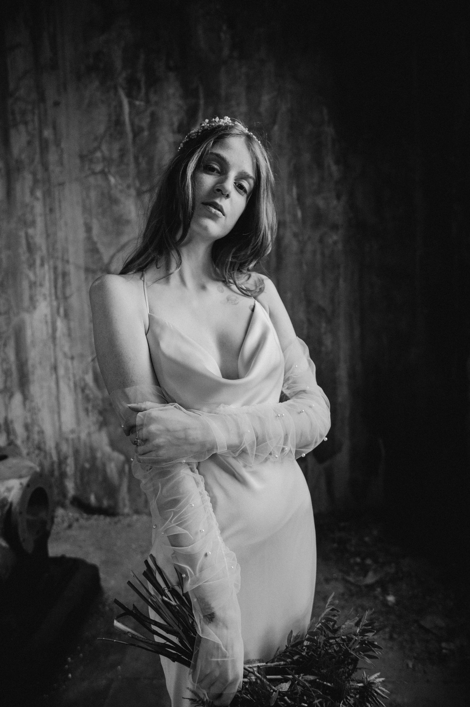 Dramatic black and white image of bride in silk gown holding bouquet against weathered wall.