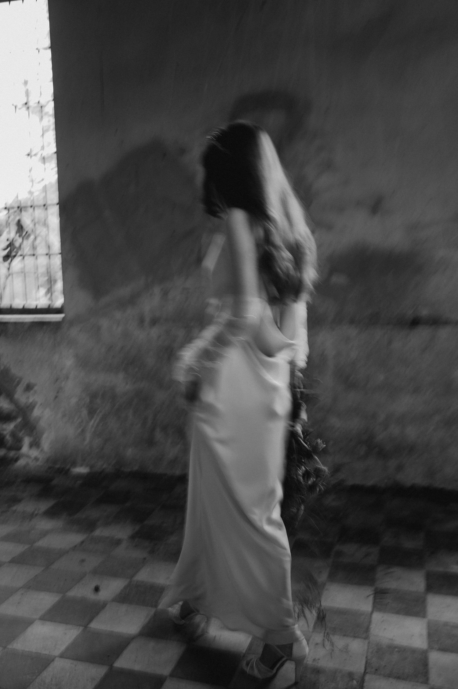 Motion-blurred black and white photo of bride dancing in vintage room with checkered floor.