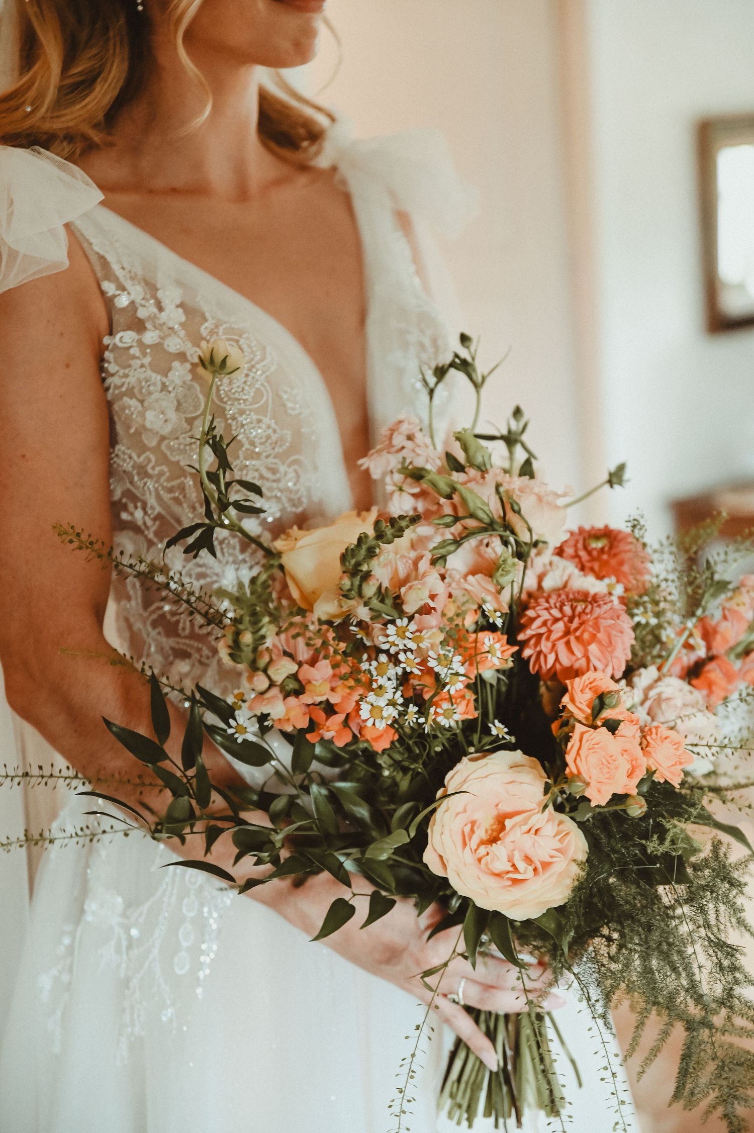 Close-up of a peach and coral wedding bouquet with delicate lace details on bridal gown.