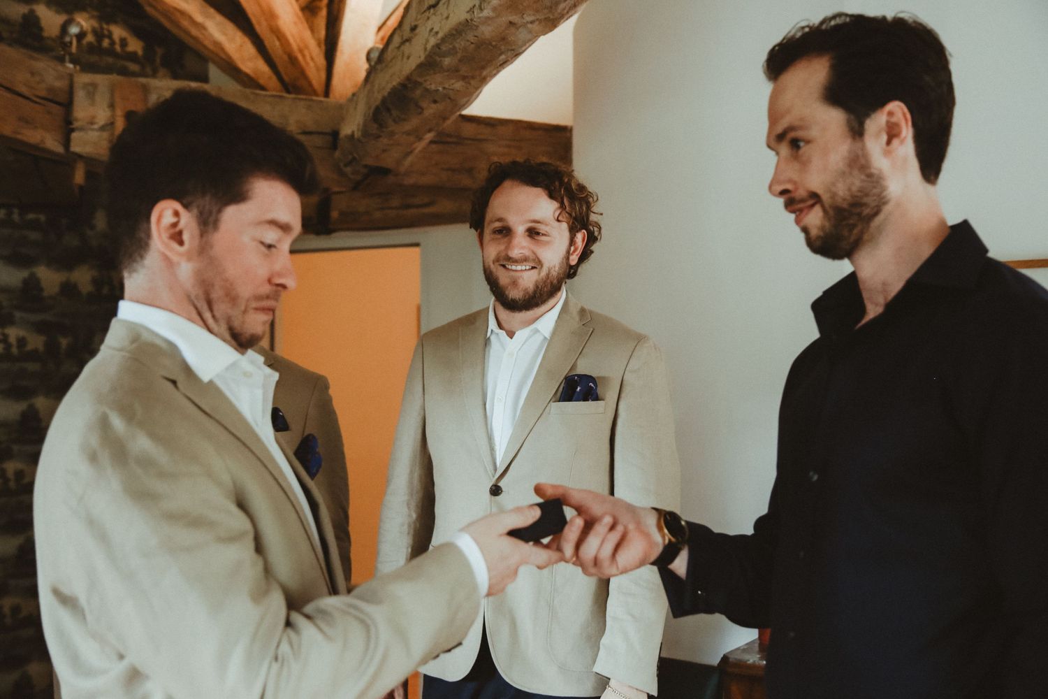 Three people share a moment while getting ready in a room with exposed brick and wooden beams.