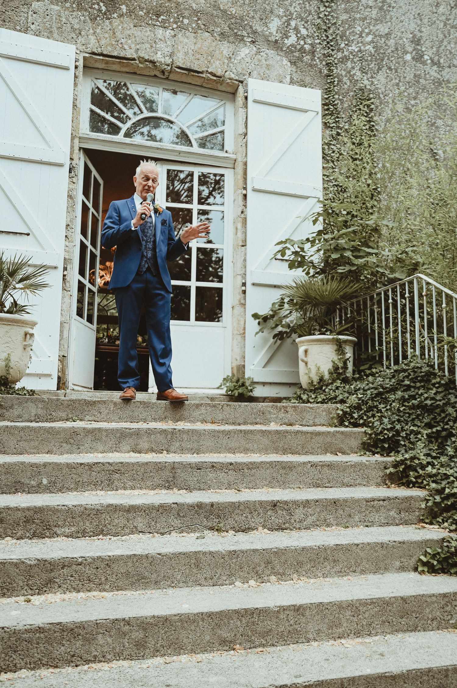 Someone in a navy suit stands on stone steps outside an elegant doorway.