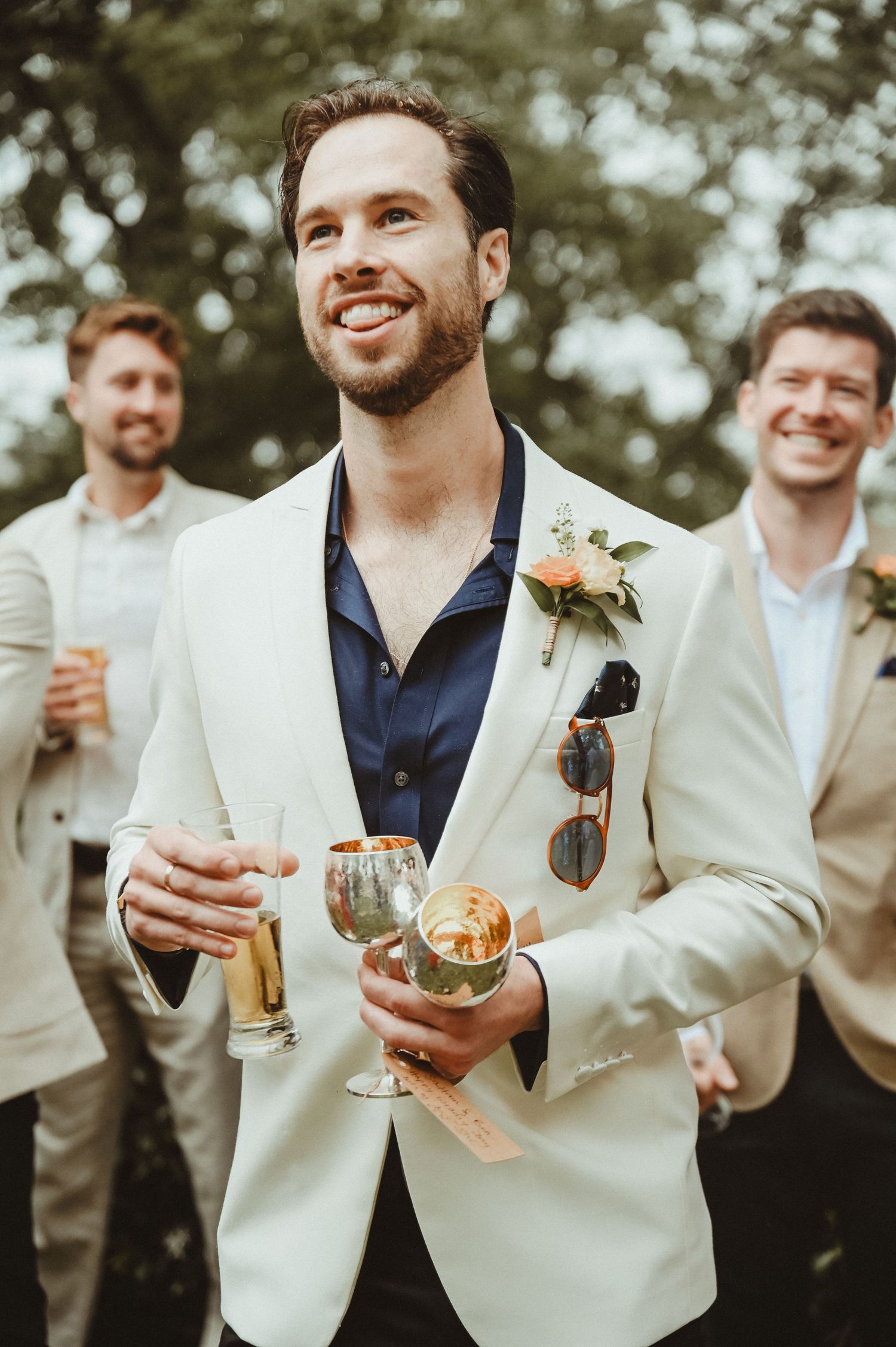 A guest in a white blazer holds drinks while enjoying the outdoor wedding reception.