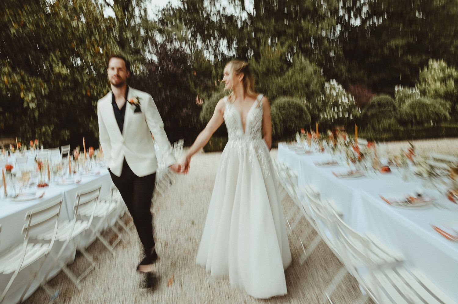 Elegant outdoor wedding reception with rows of white chairs and tables along a garden path.