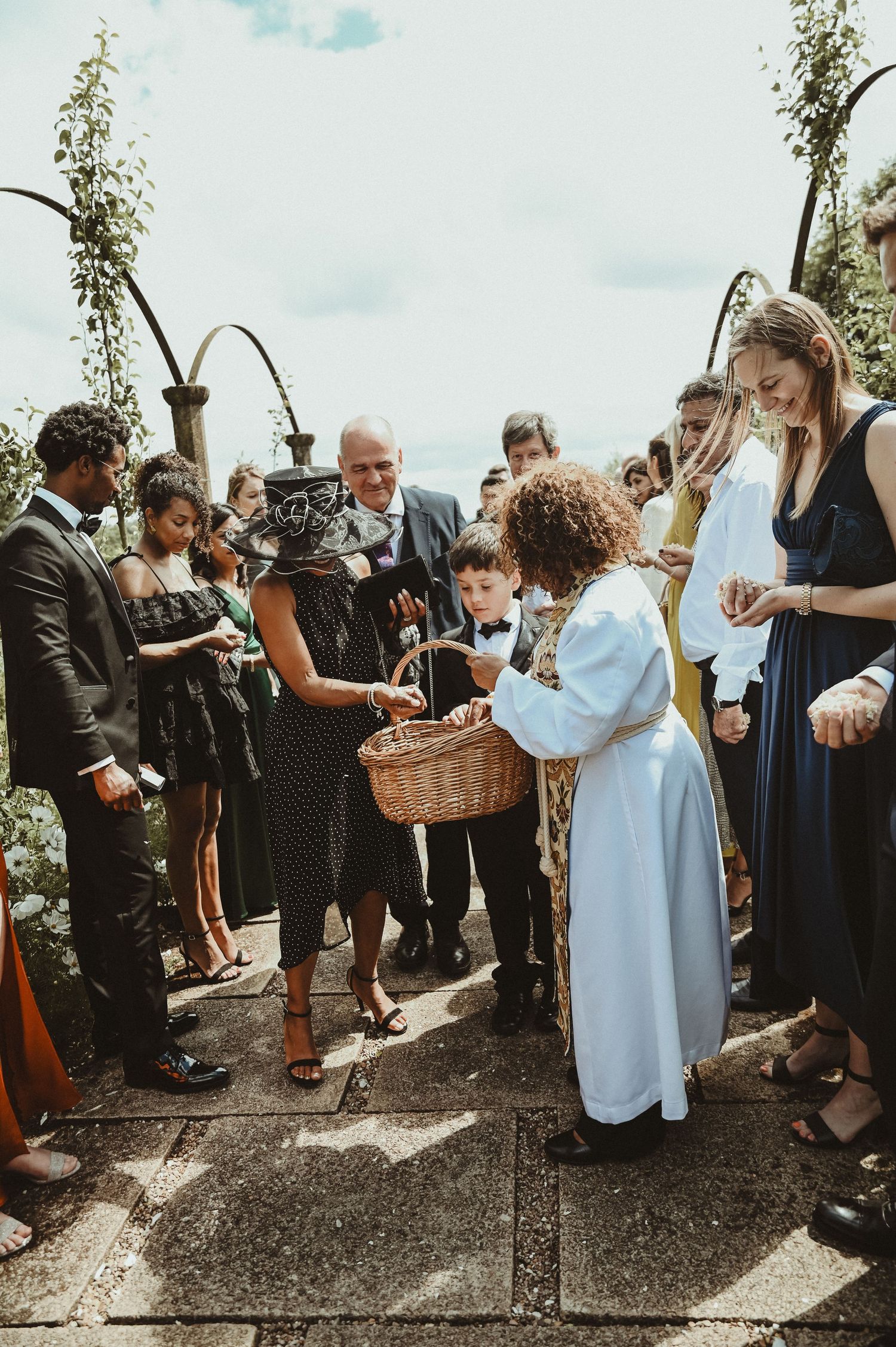 A group of wedding guests gather around a wicker basket during an outdoor celebration.