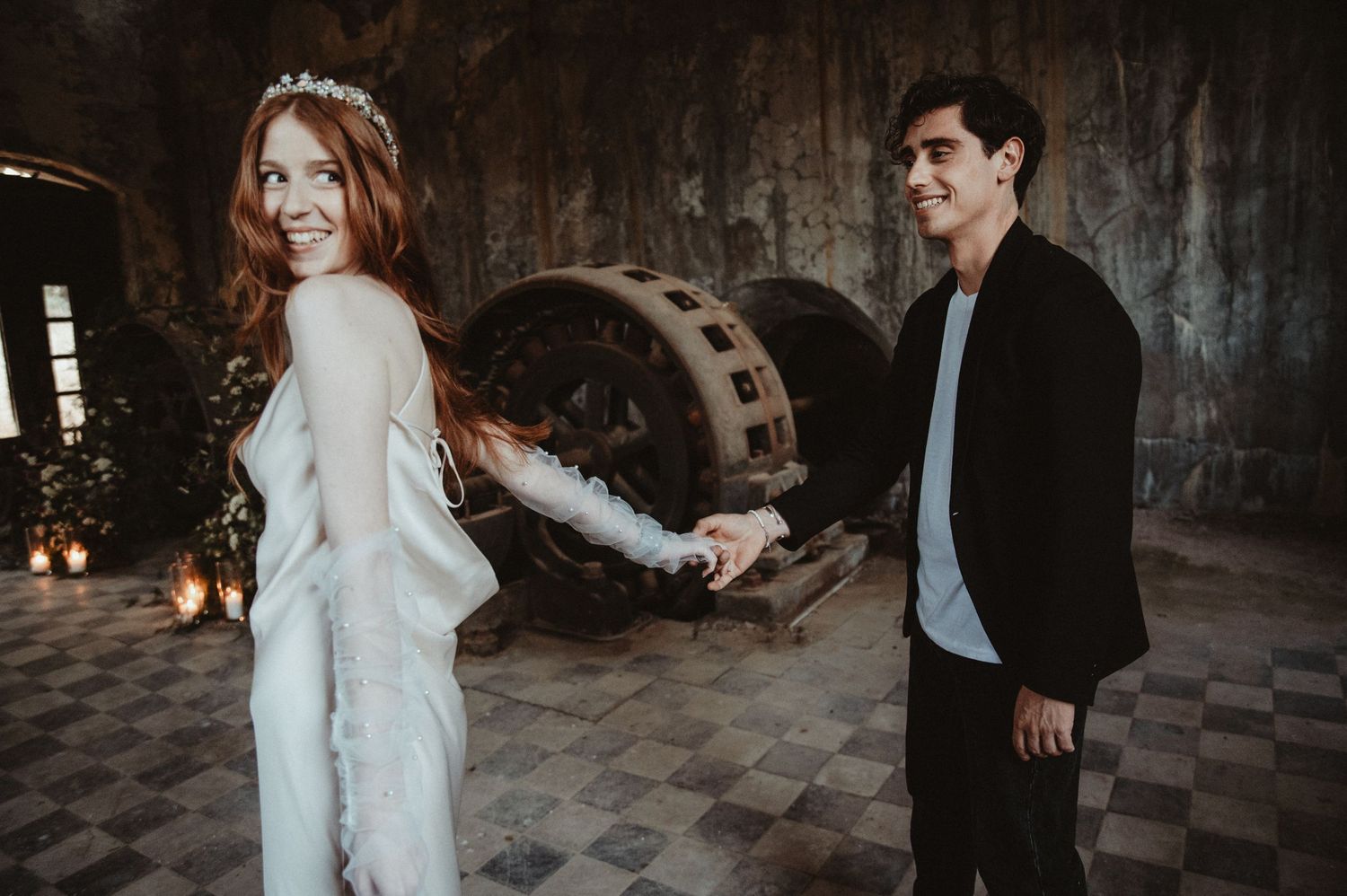A couple poses in an industrial space with rustic machinery and candlelit ambiance.