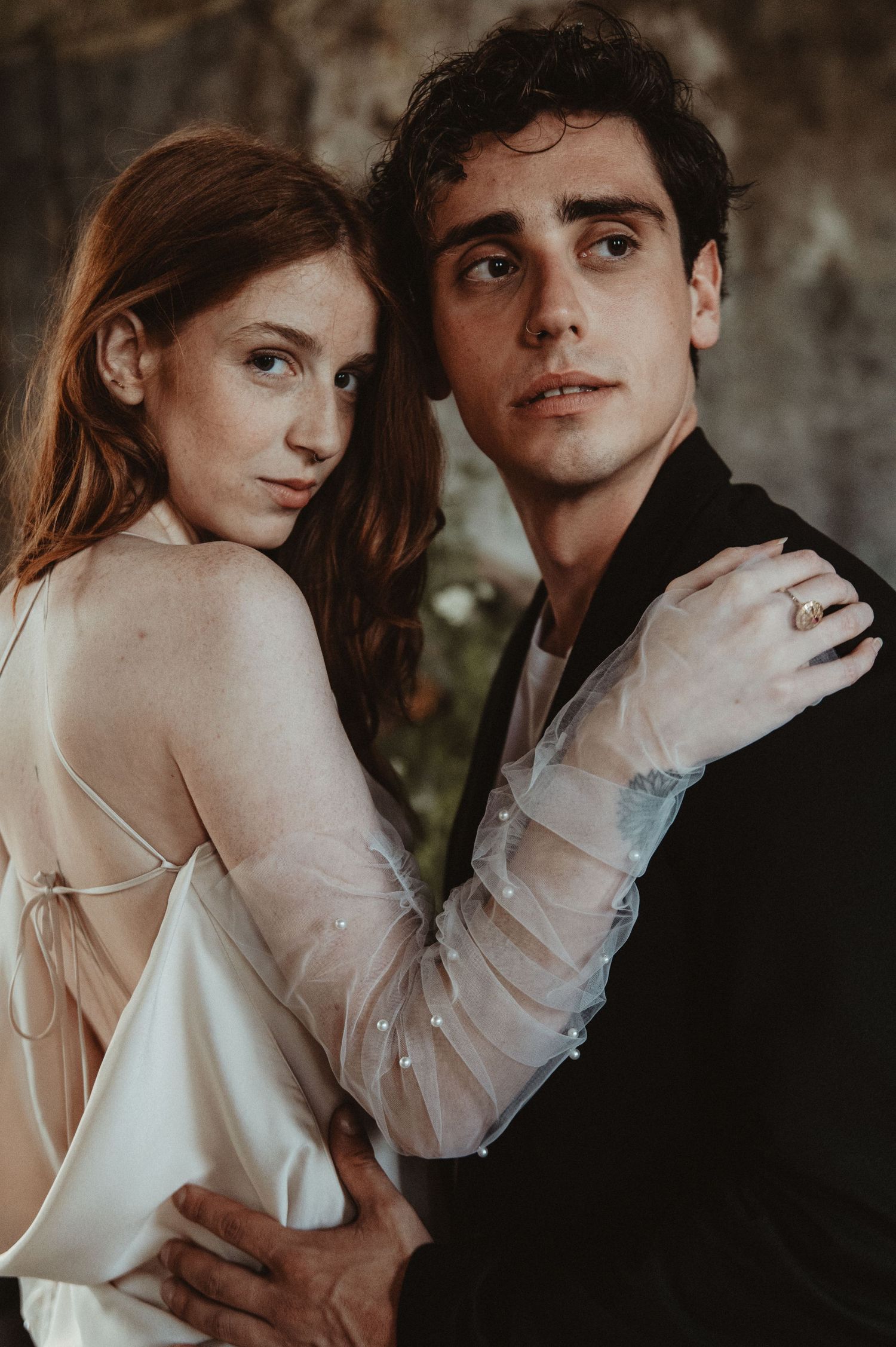 Artistic wedding photography showing a couple in elegant attire against a textured wall.