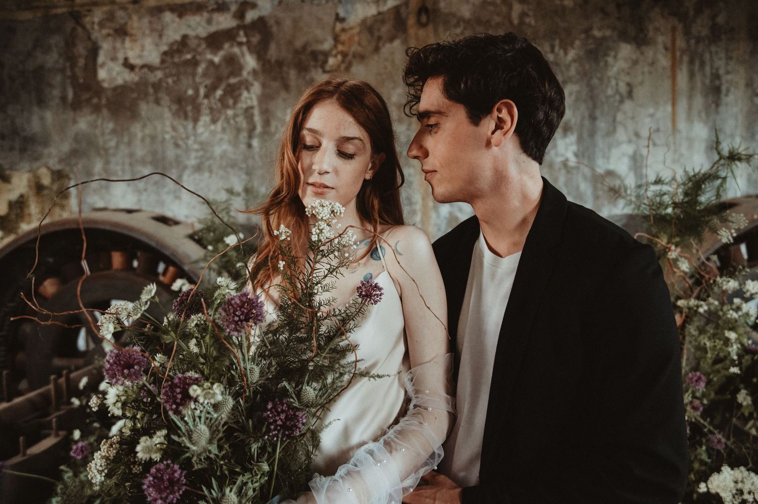 Intimate couple portrait in rustic setting with delicate floral bouquet.
