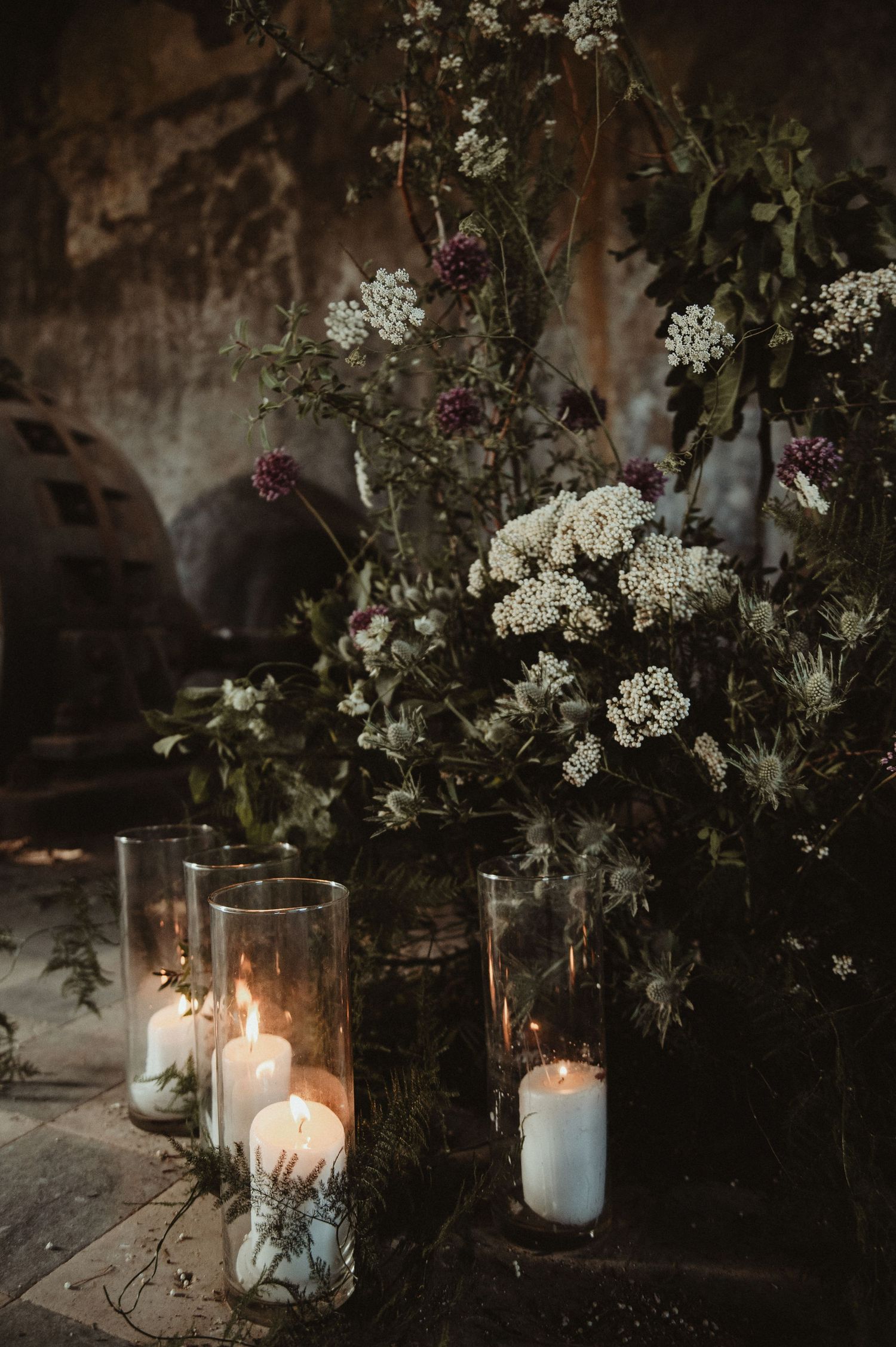 Romantic floral arrangement with white blooms and glowing candles in glass holders.