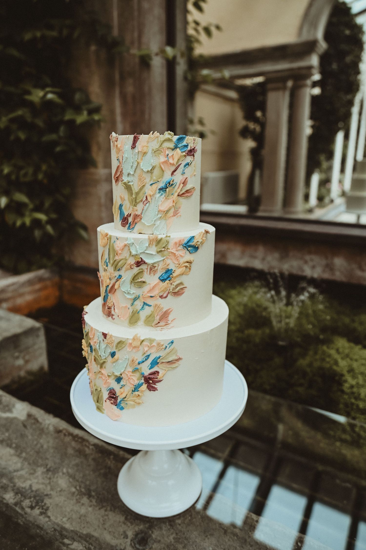 A three-tiered white wedding cake decorated with watercolor-style blue and copper brushstrokes.
