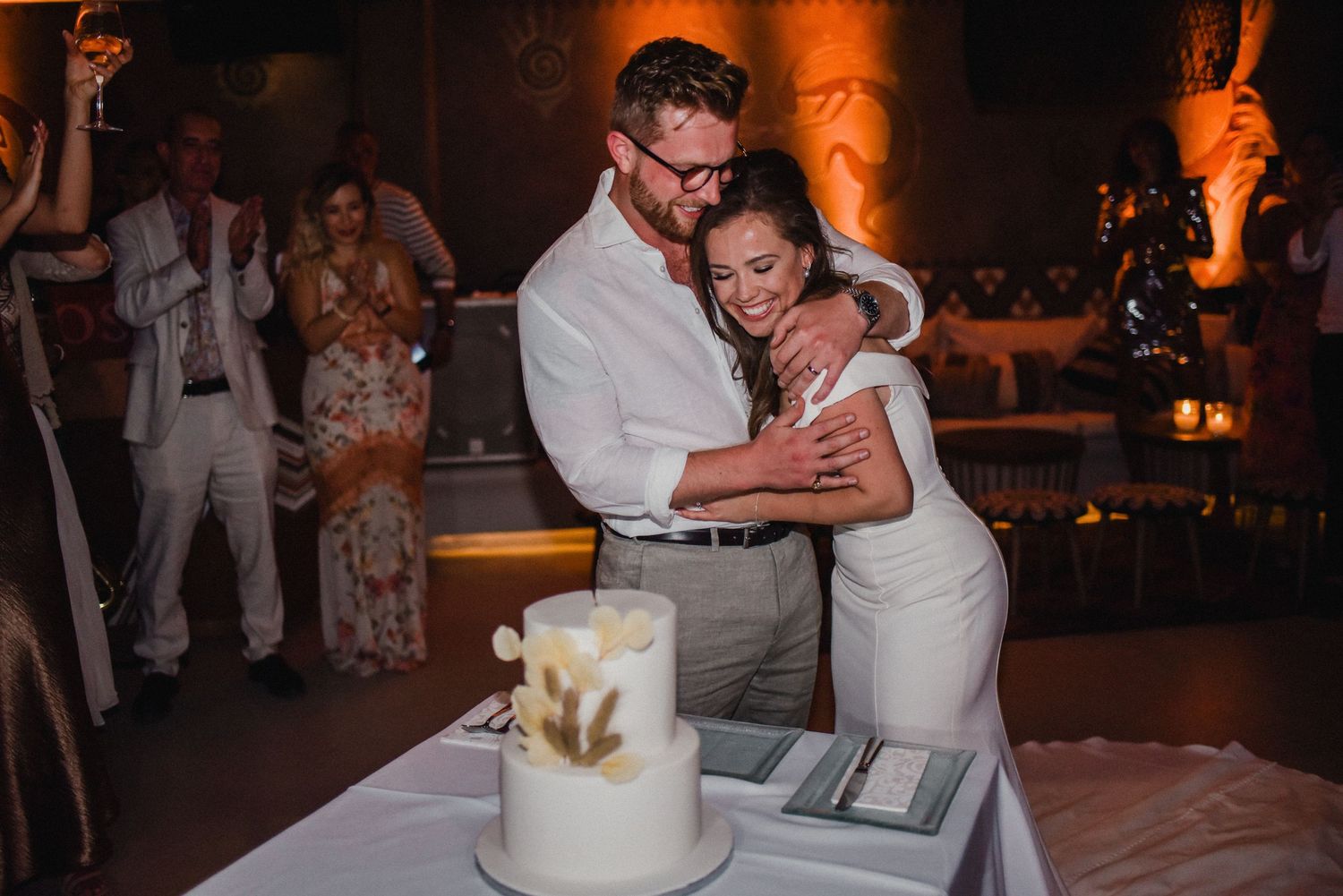 A couple embraces while celebrating with their wedding cake at an intimate reception.