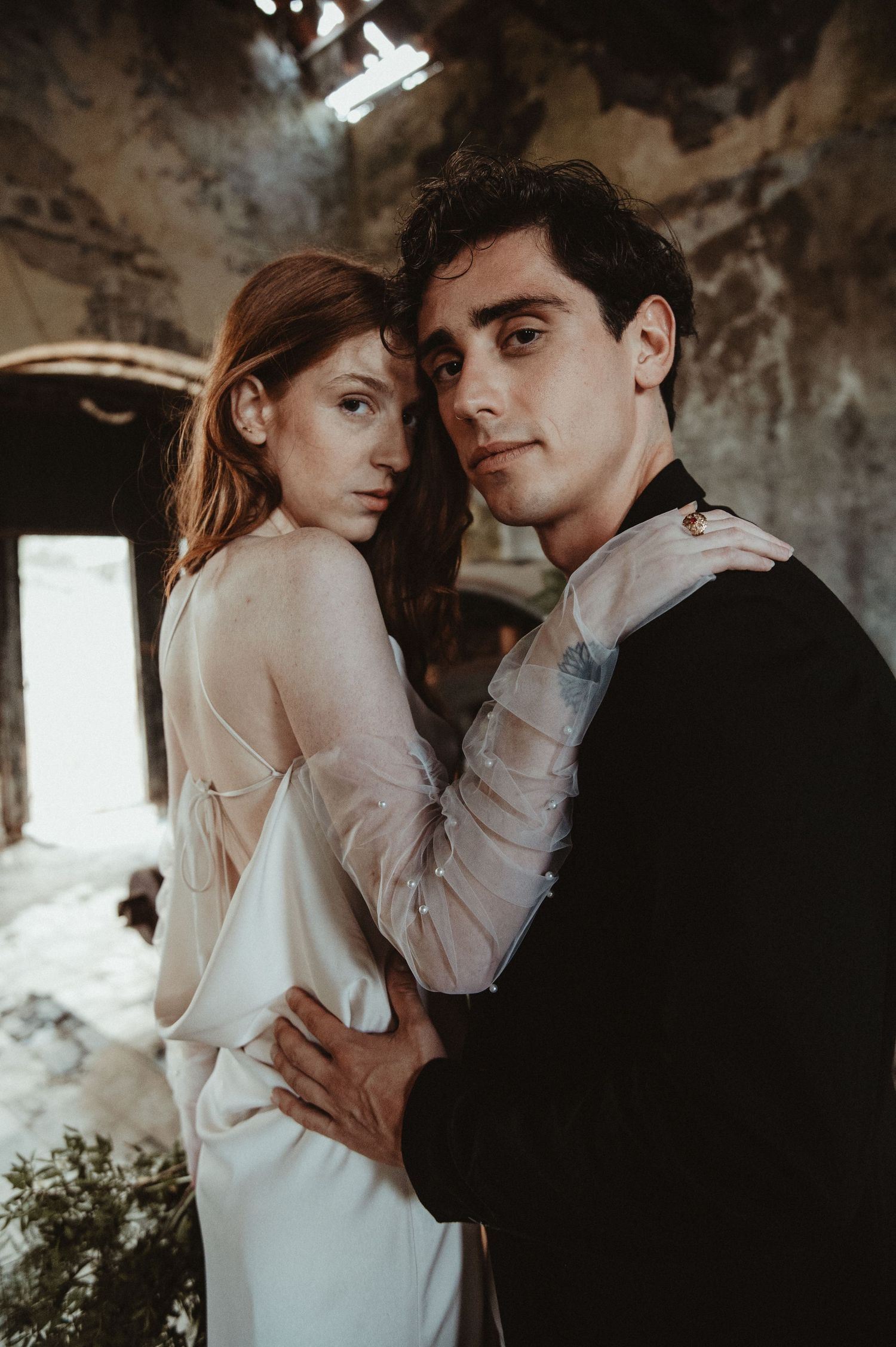 Moody wedding portrait in a rustic setting with dramatic window lighting.
