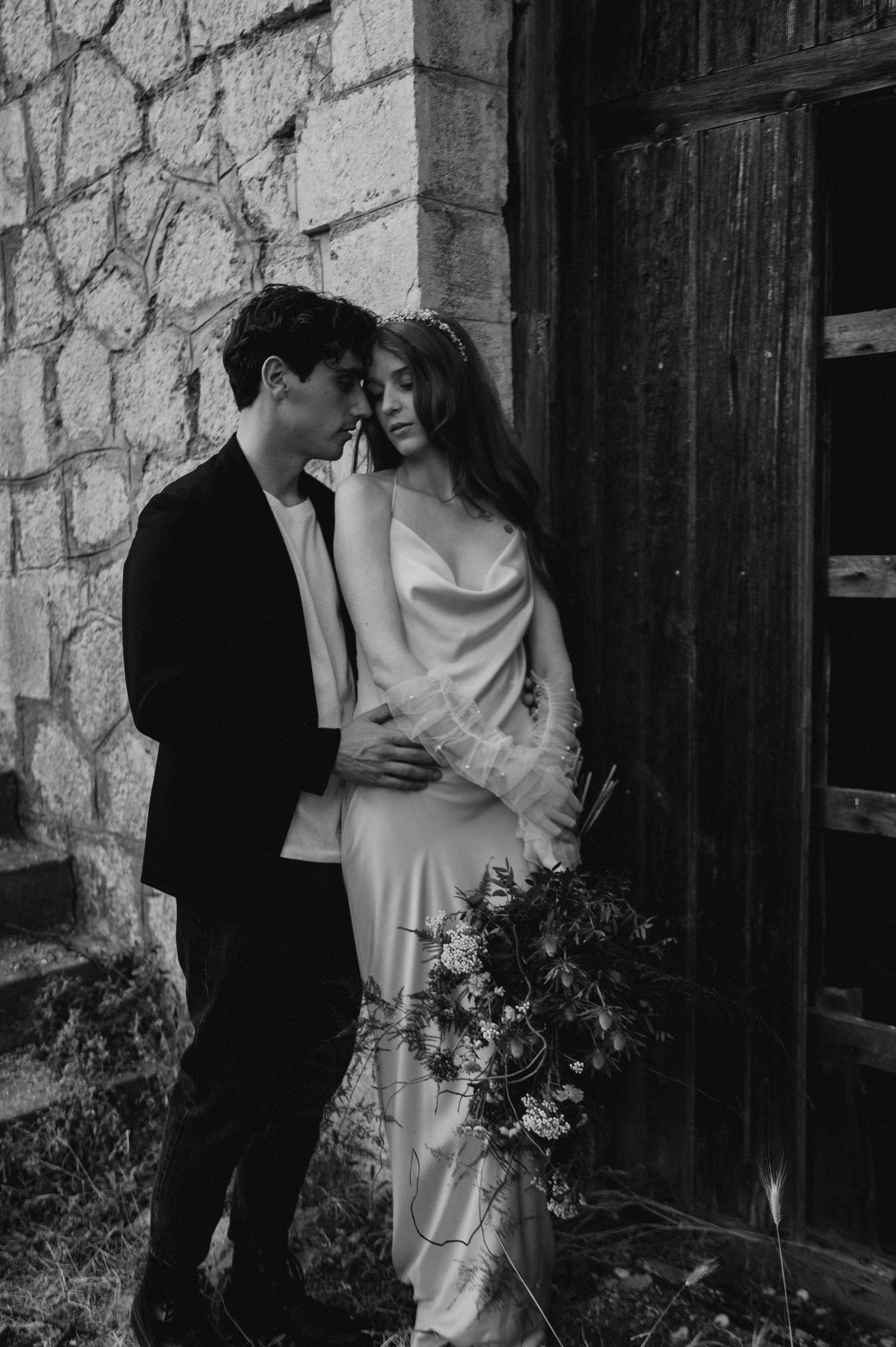 A romantic moment shared against a rustic stone wall and wooden door.