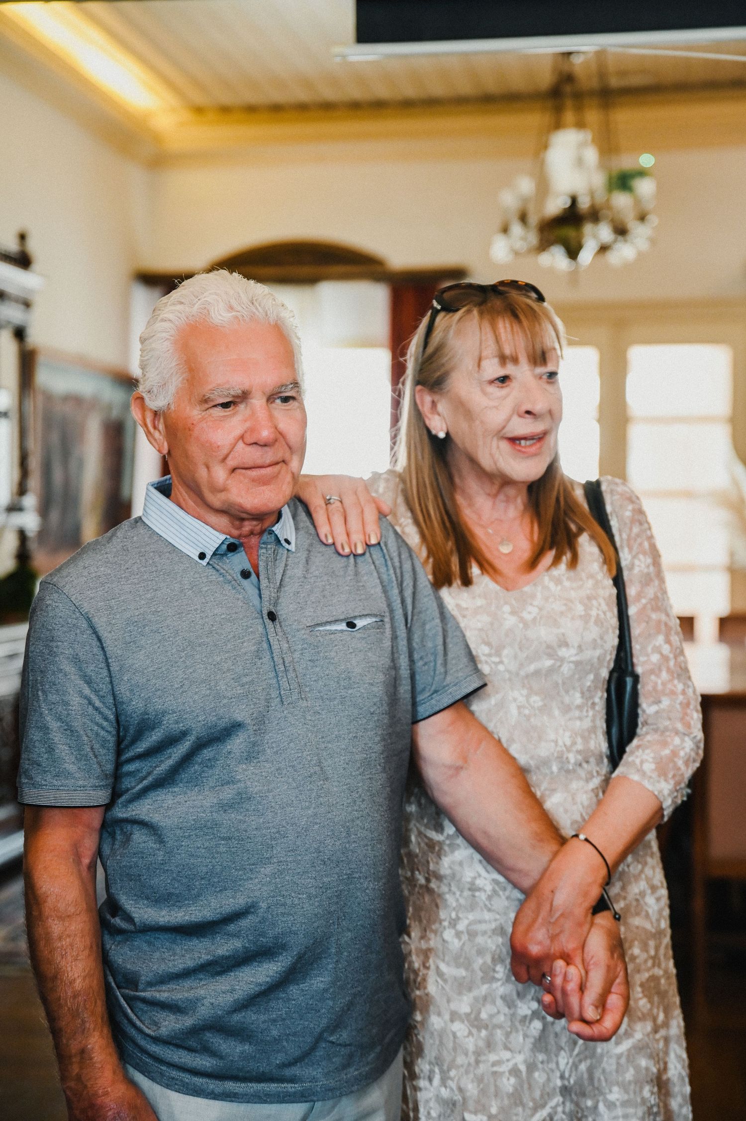 A couple stands together in a room with a chandelier.