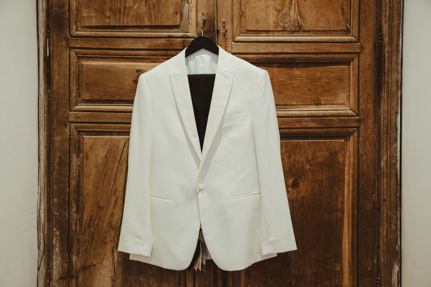 White formal blazer hanging on wooden door showing wedding day attire.