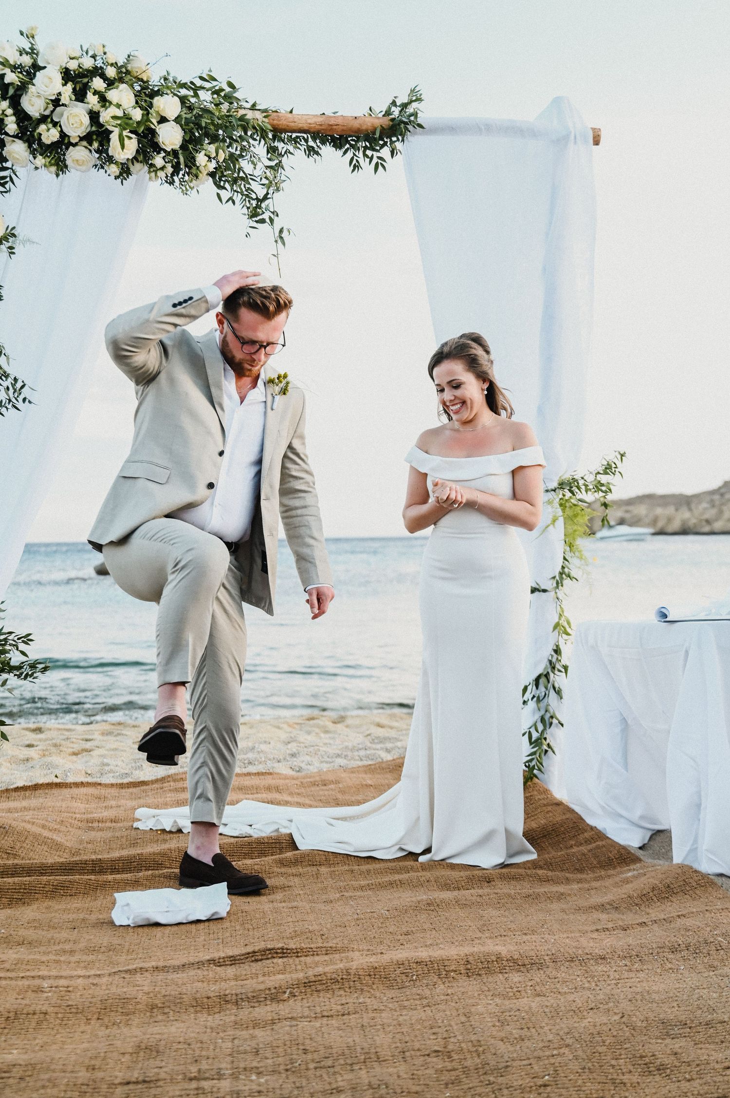Couple shares joyful moment under floral arch during beach wedding ceremony.