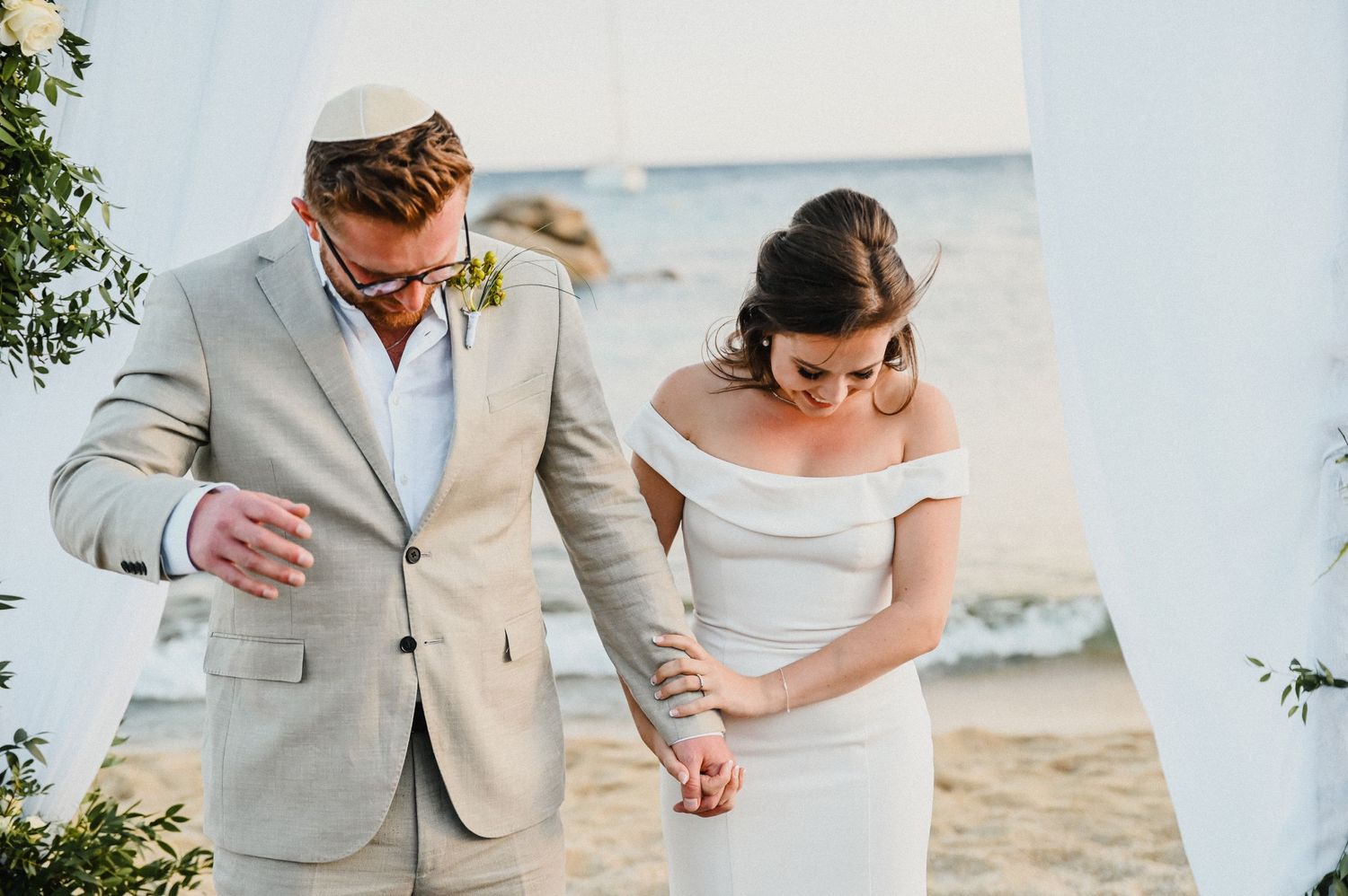Candid moment during beach wedding ceremony under white draped arch with flowers.
