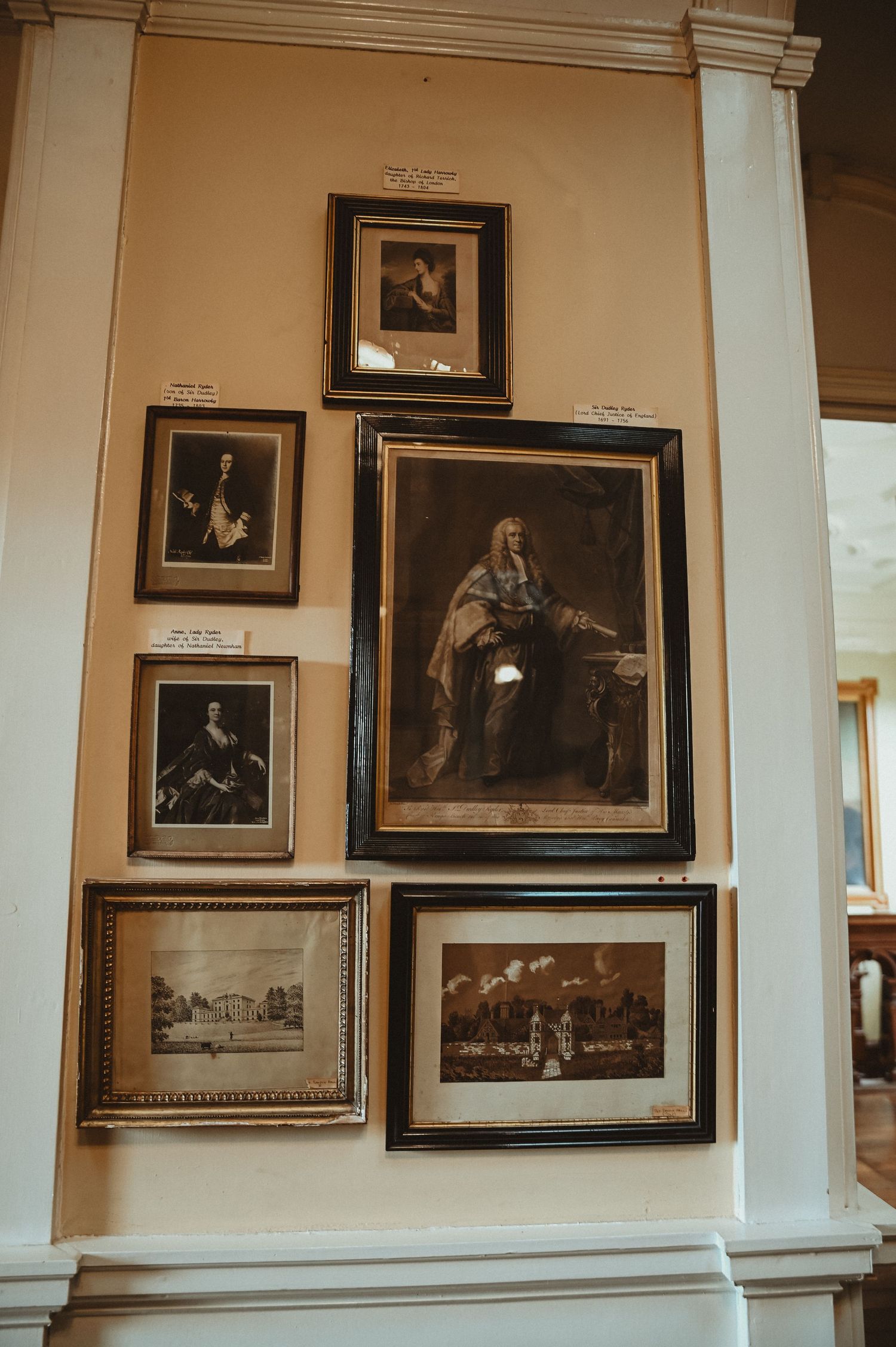 Collection of vintage portraits and artwork arranged on a cream-colored wall with classical molding.