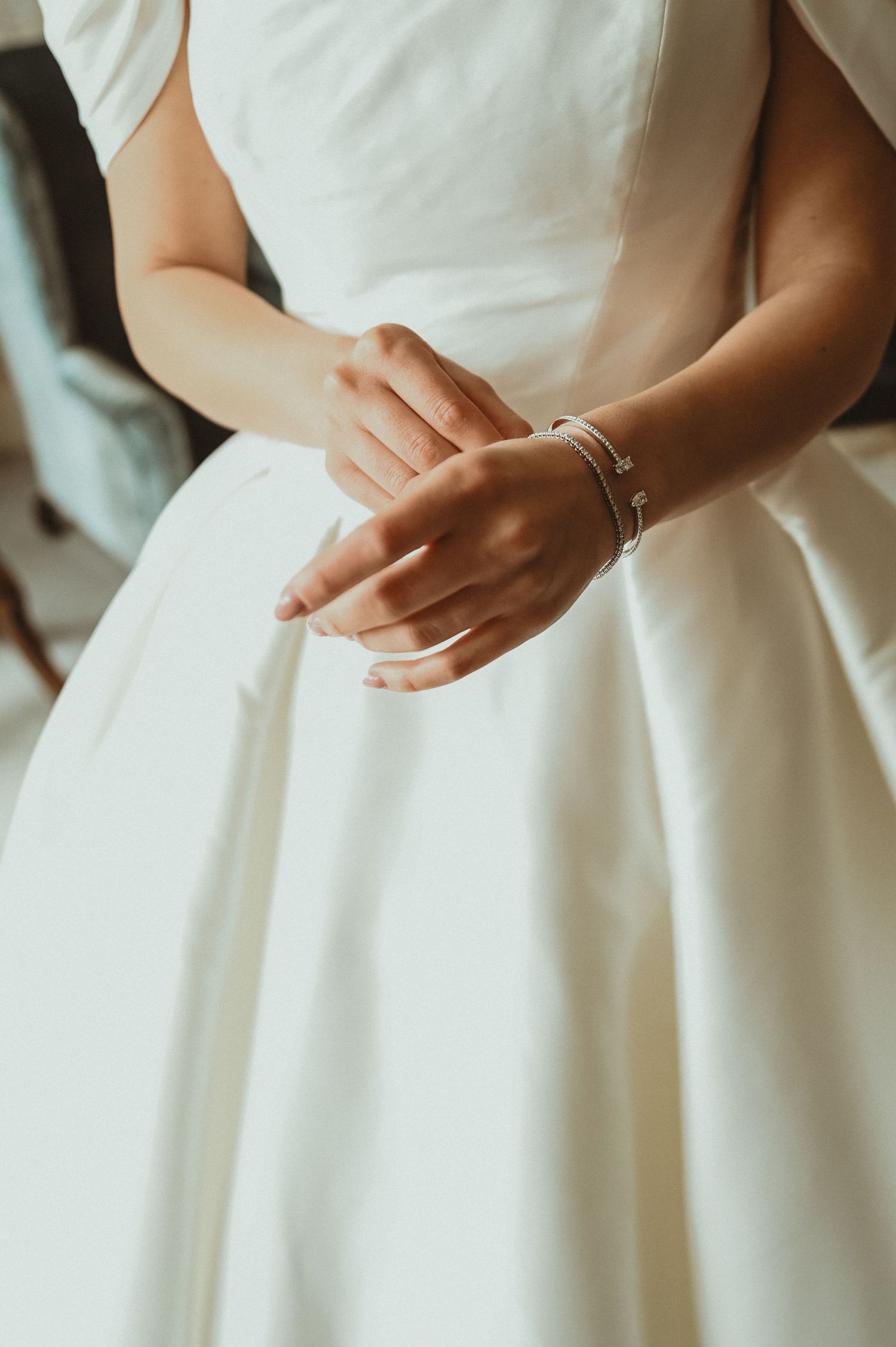 Detail shot of hands wearing wedding rings and bracelet against a white wedding dress.