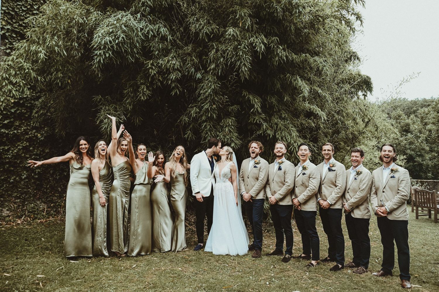 Wedding party strikes fun poses outdoors with bridesmaids and groomsmen in coordinated colors.