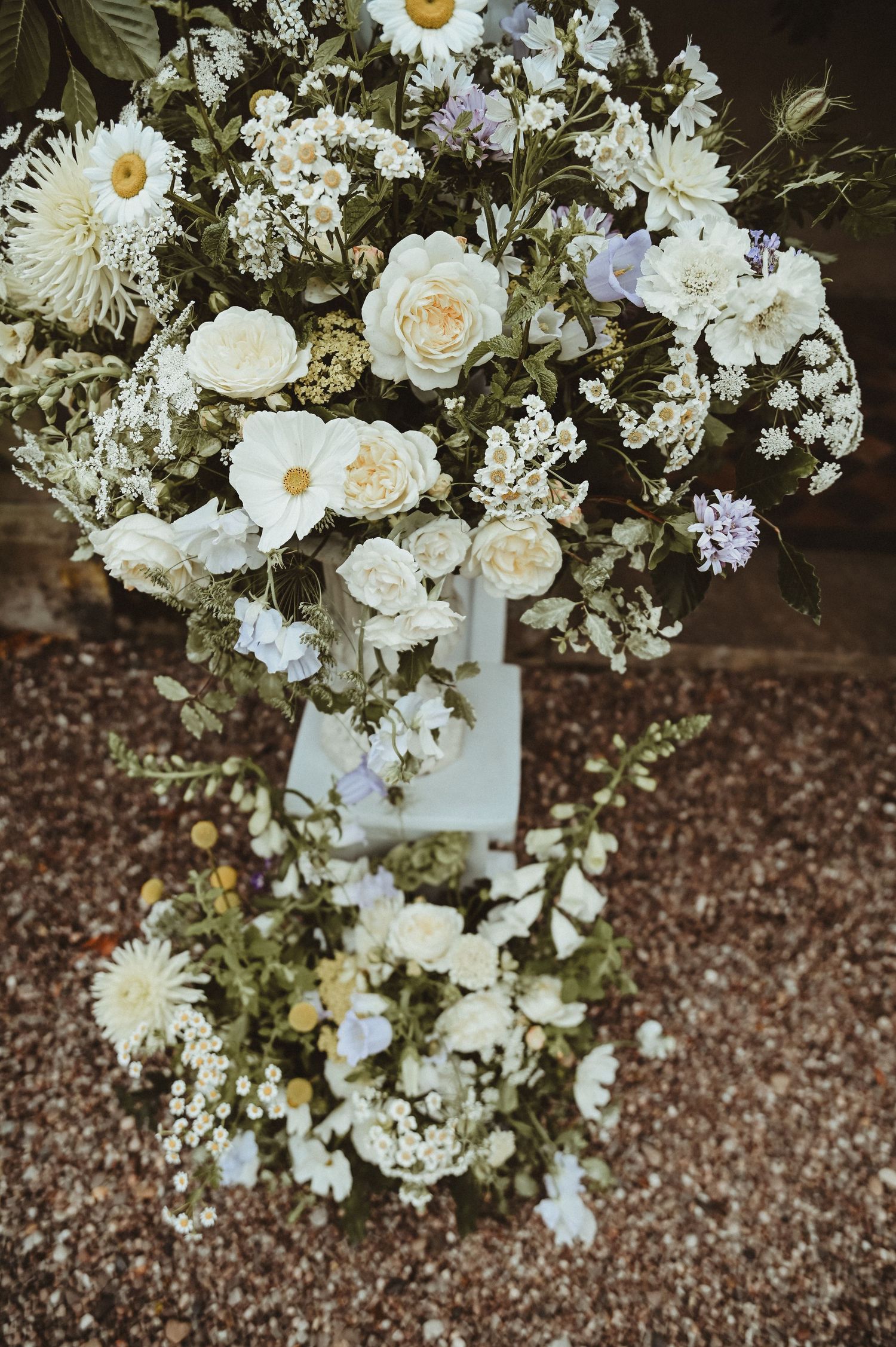An elegant white and purple floral arrangement with daisies and roses in a garden setting.