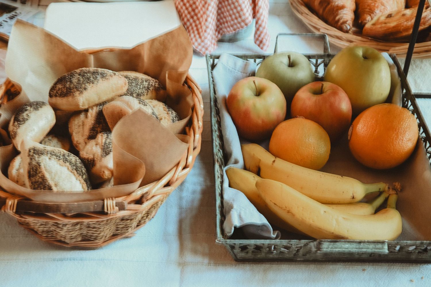 Fresh bread basket and colorful fruits including apples, oranges and bananas arranged on white surface.