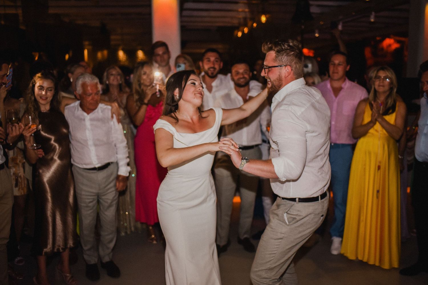Wedding celebration on the dance floor with guests watching in dimly lit venue.