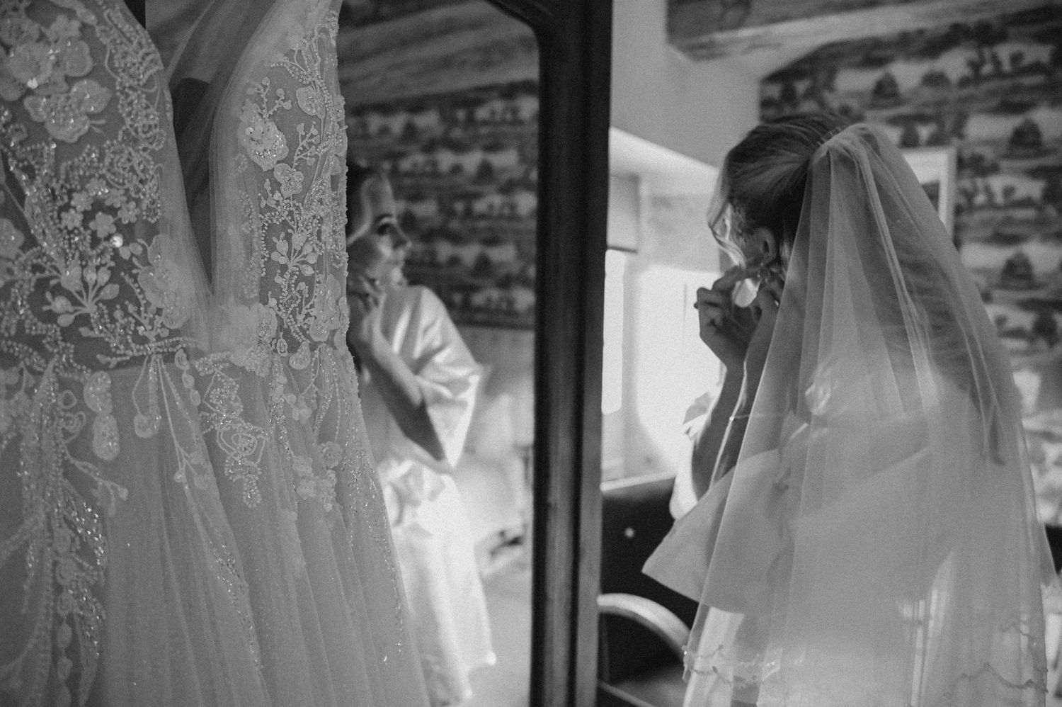 Black and white photo of wedding dress and veil preparations in vintage setting.