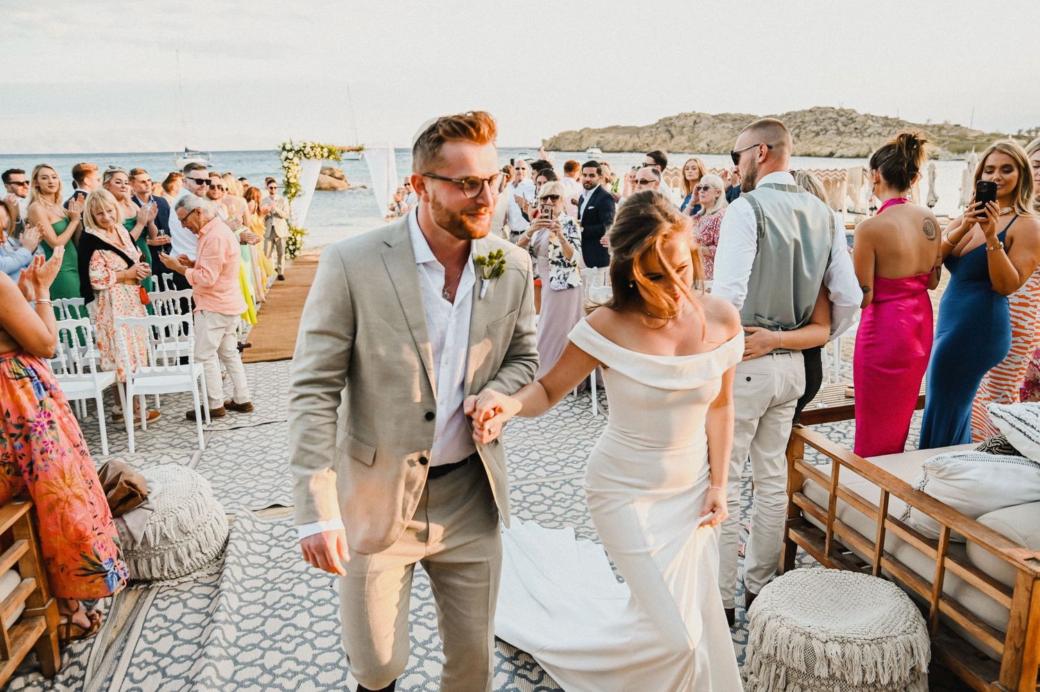 A couple celebrating during their beach wedding ceremony with guests looking on in the background.