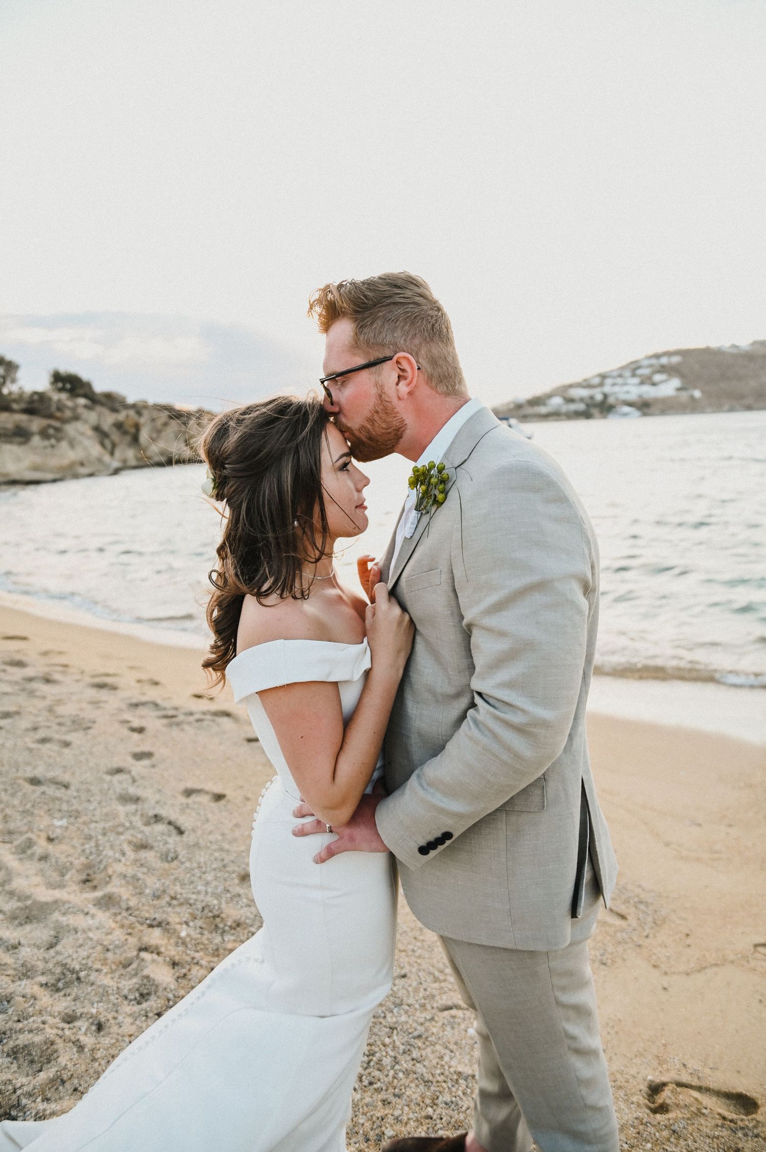 Intimate wedding portrait of couple embracing on beach with ocean waves in background.