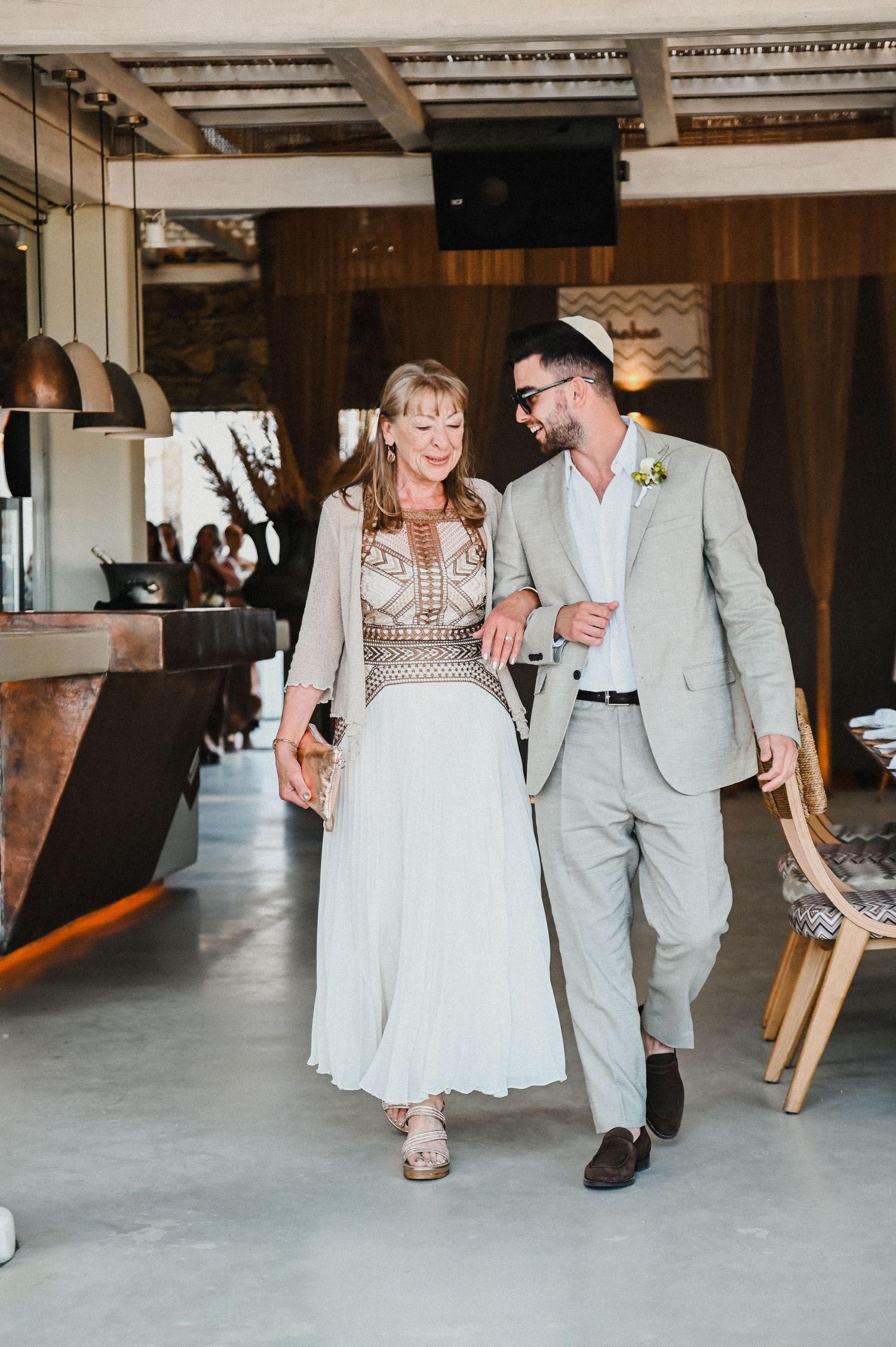 A couple walks together in modern wedding attire through an industrial-style venue.