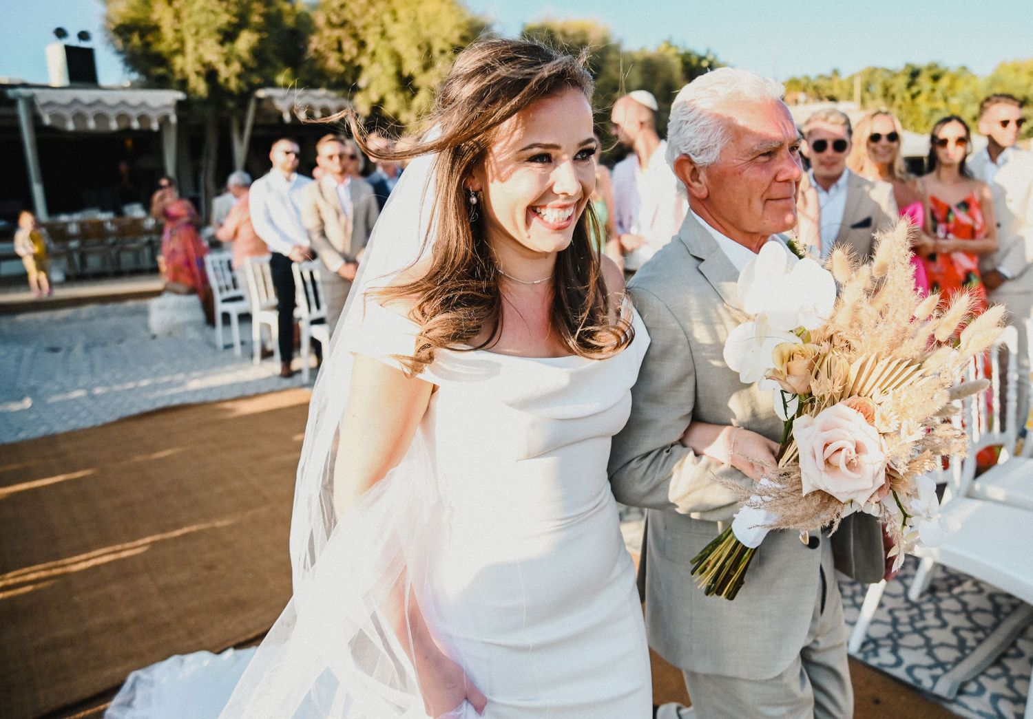 Joyful wedding procession moment captured in warm sunlight with dried flower bouquet.