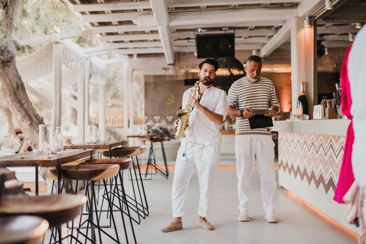 Two servers in white uniforms carrying trays in a modern restaurant setting.