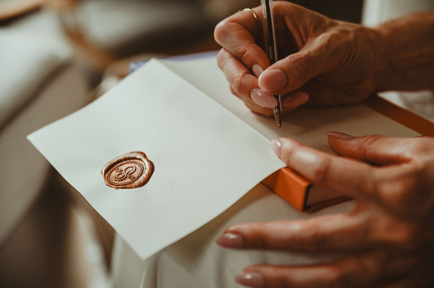 Hands writing on a white paper with a red wax seal visible.