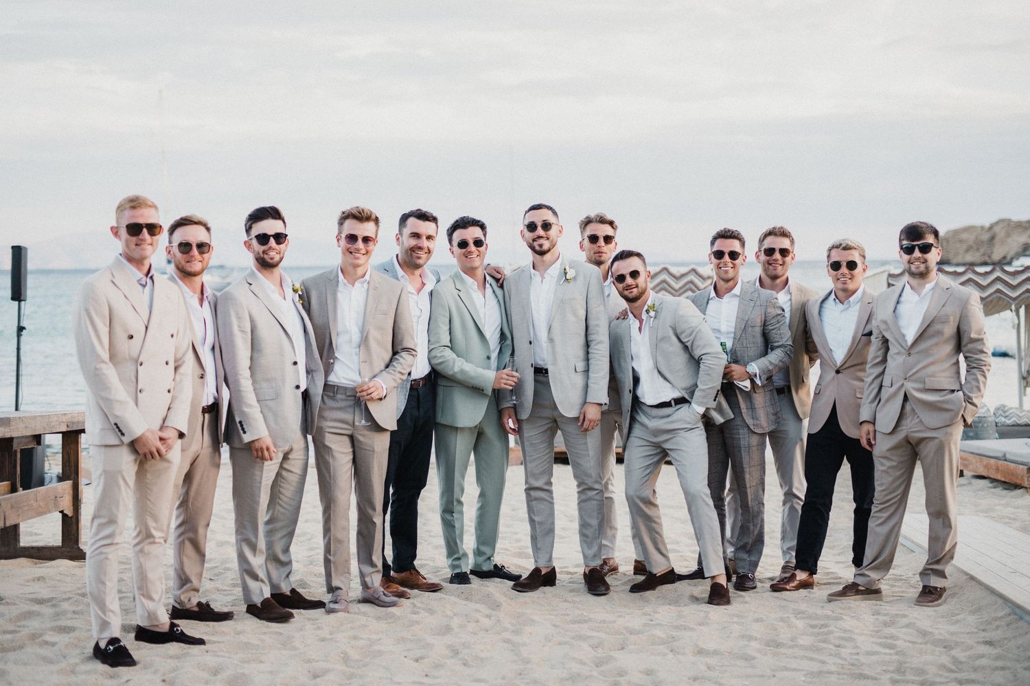 Groomsmen in light suits posing together on oceanfront deck.