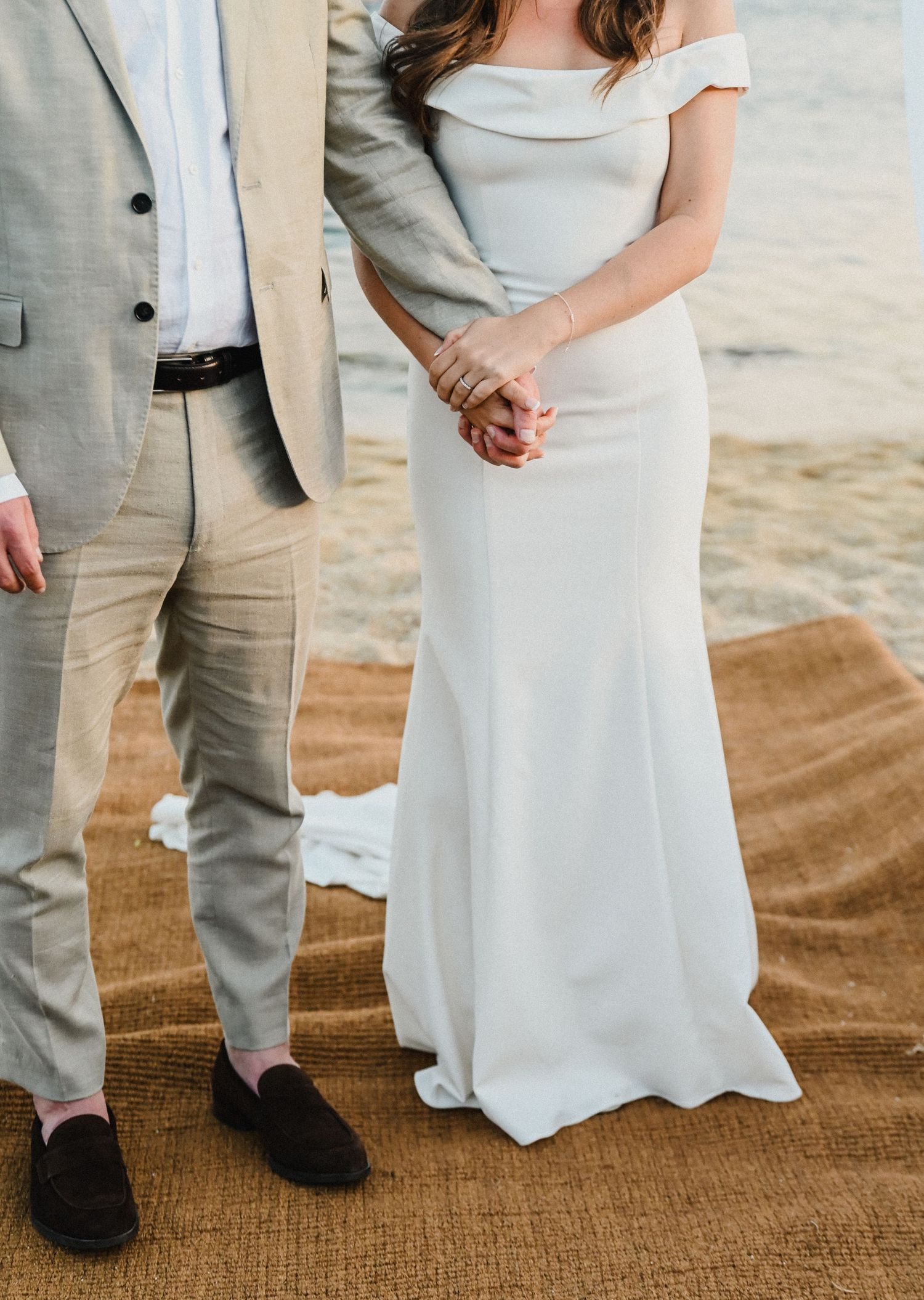 Close-up of couple's formal attire showing light gray suit and flowing white wedding dress on beach.