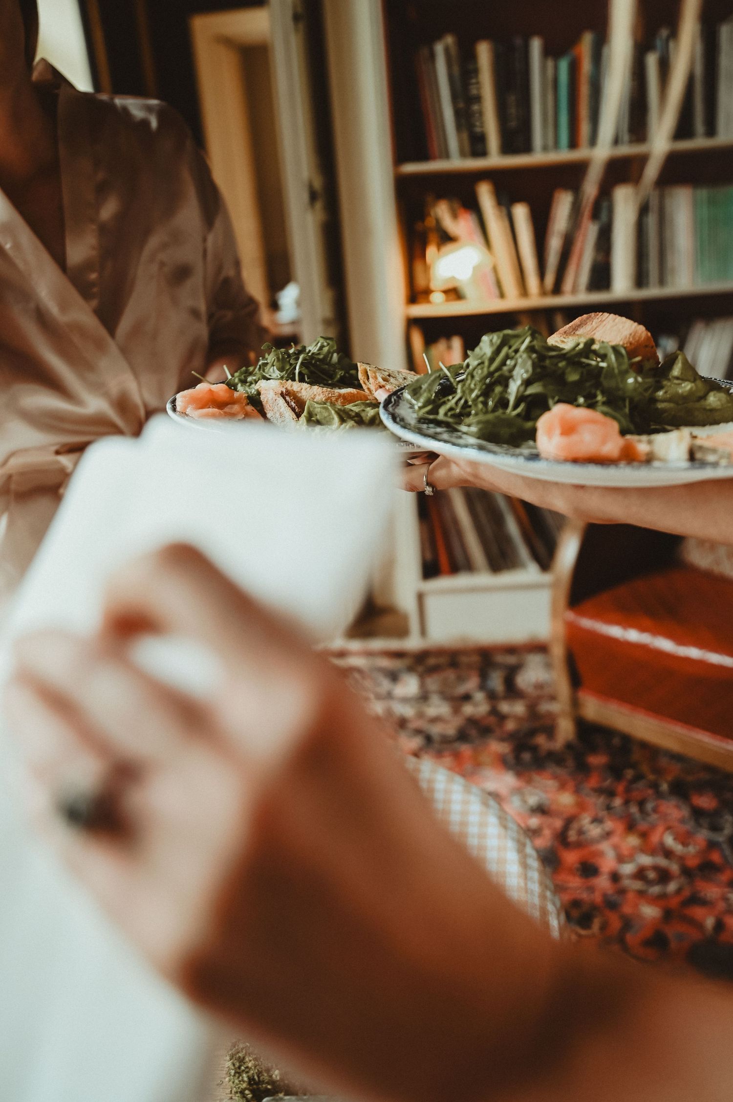 Close-up of hands serving plates of fresh salad and appetizers.