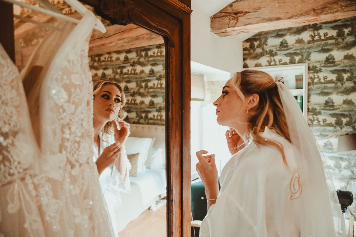 Wedding preparations scene with white dress and robe reflected in rustic room mirror.
