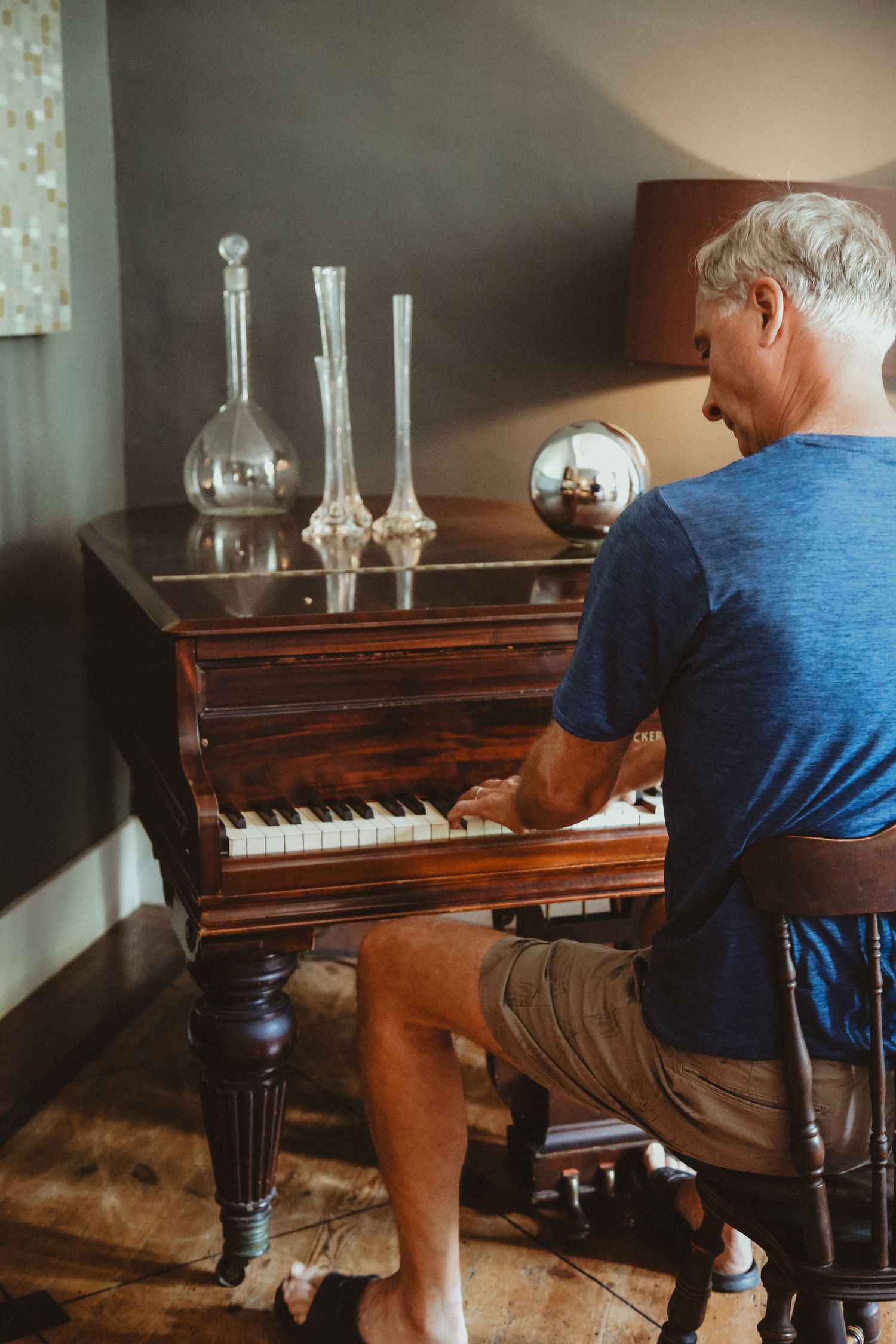 Person in blue shirt plays piano next to decorative glass vessels on wooden surface.