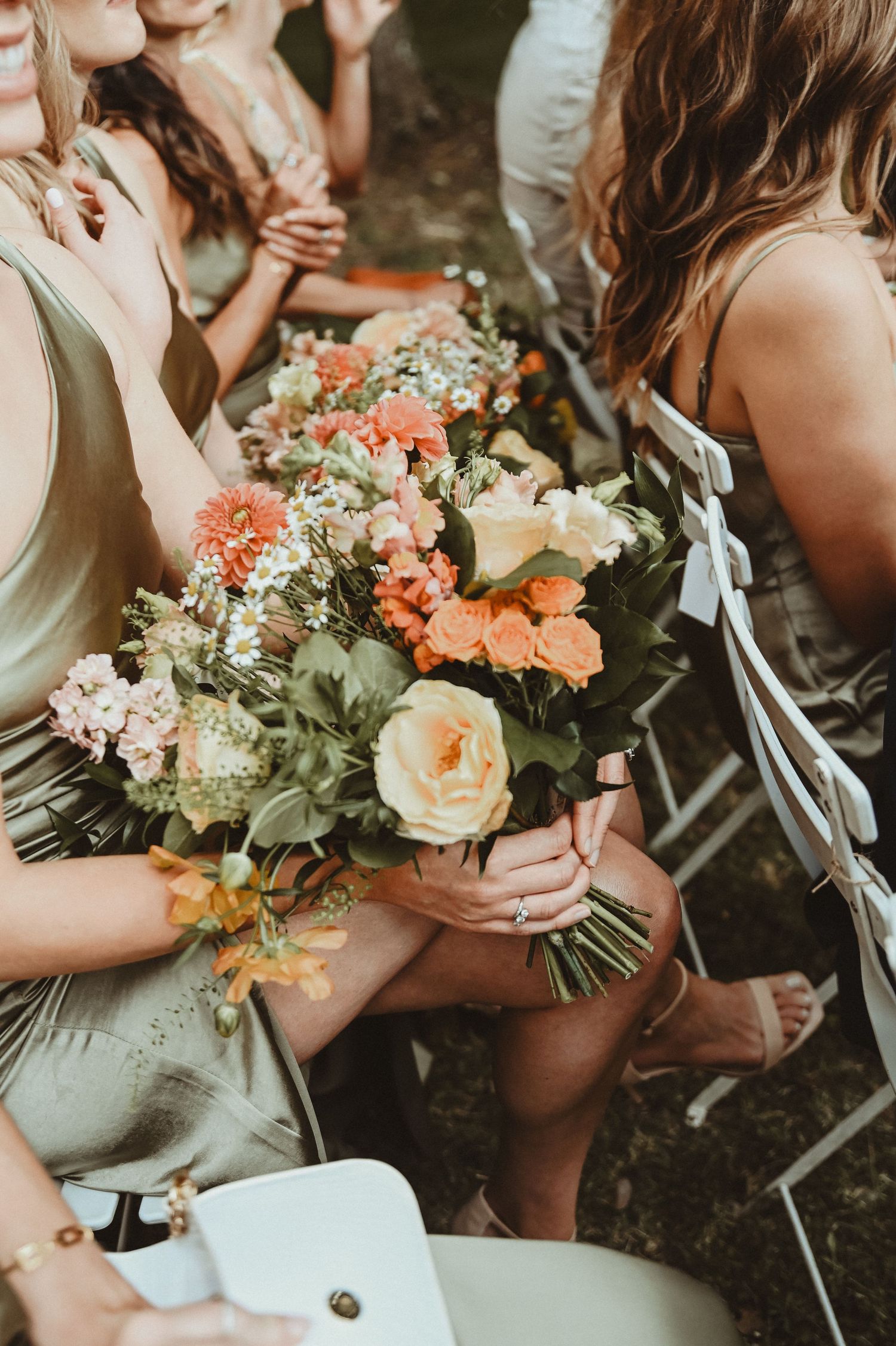 Close-up of bridesmaids holding peach and coral floral bouquets at outdoor wedding.