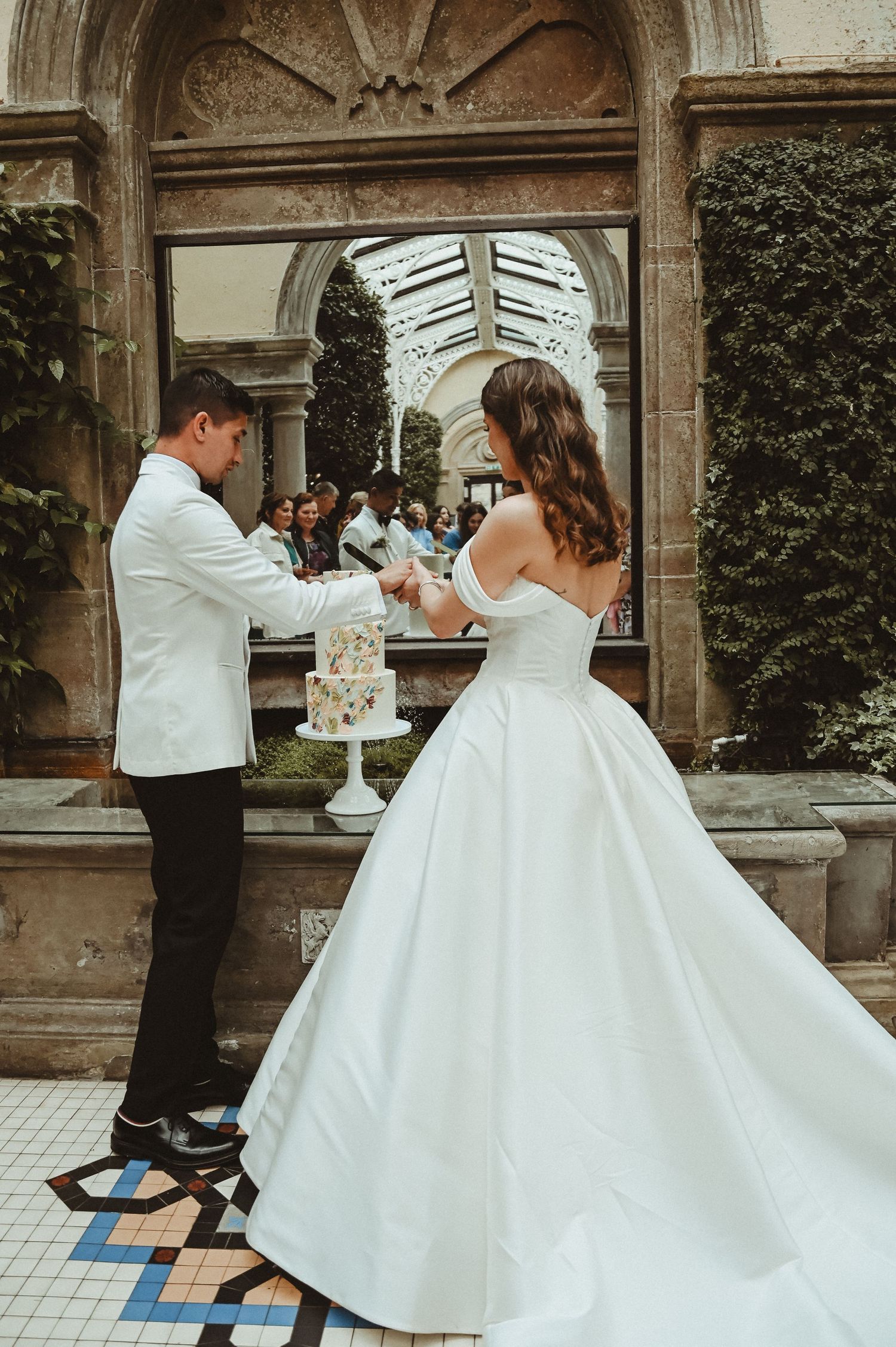 Couple cutting their wedding cake together in an ornate conservatory setting.