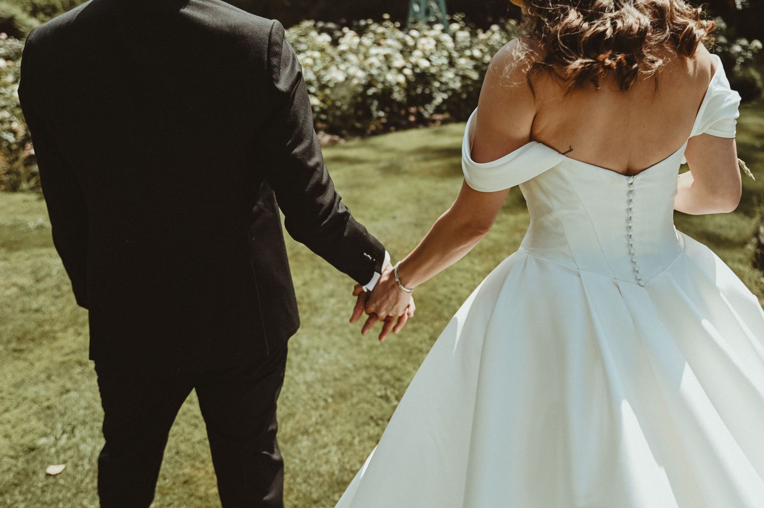 Detail shot of a classic white wedding dress with off-shoulder design in a garden setting.