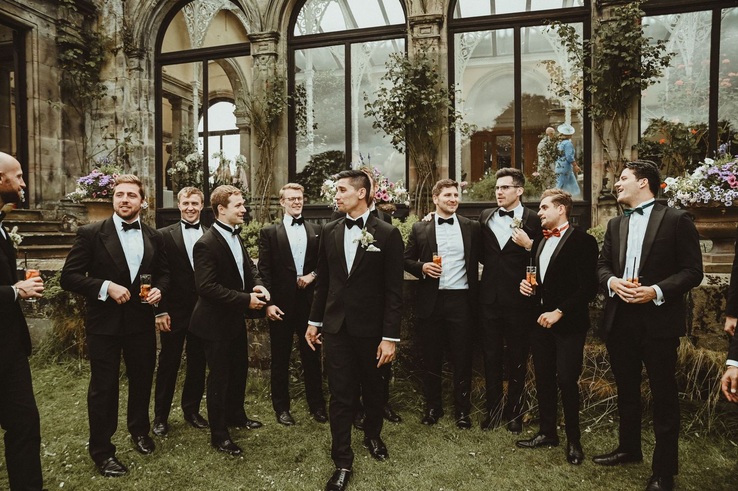 A group in black tuxedos poses for a celebratory photo in an ornate glass-enclosed garden.