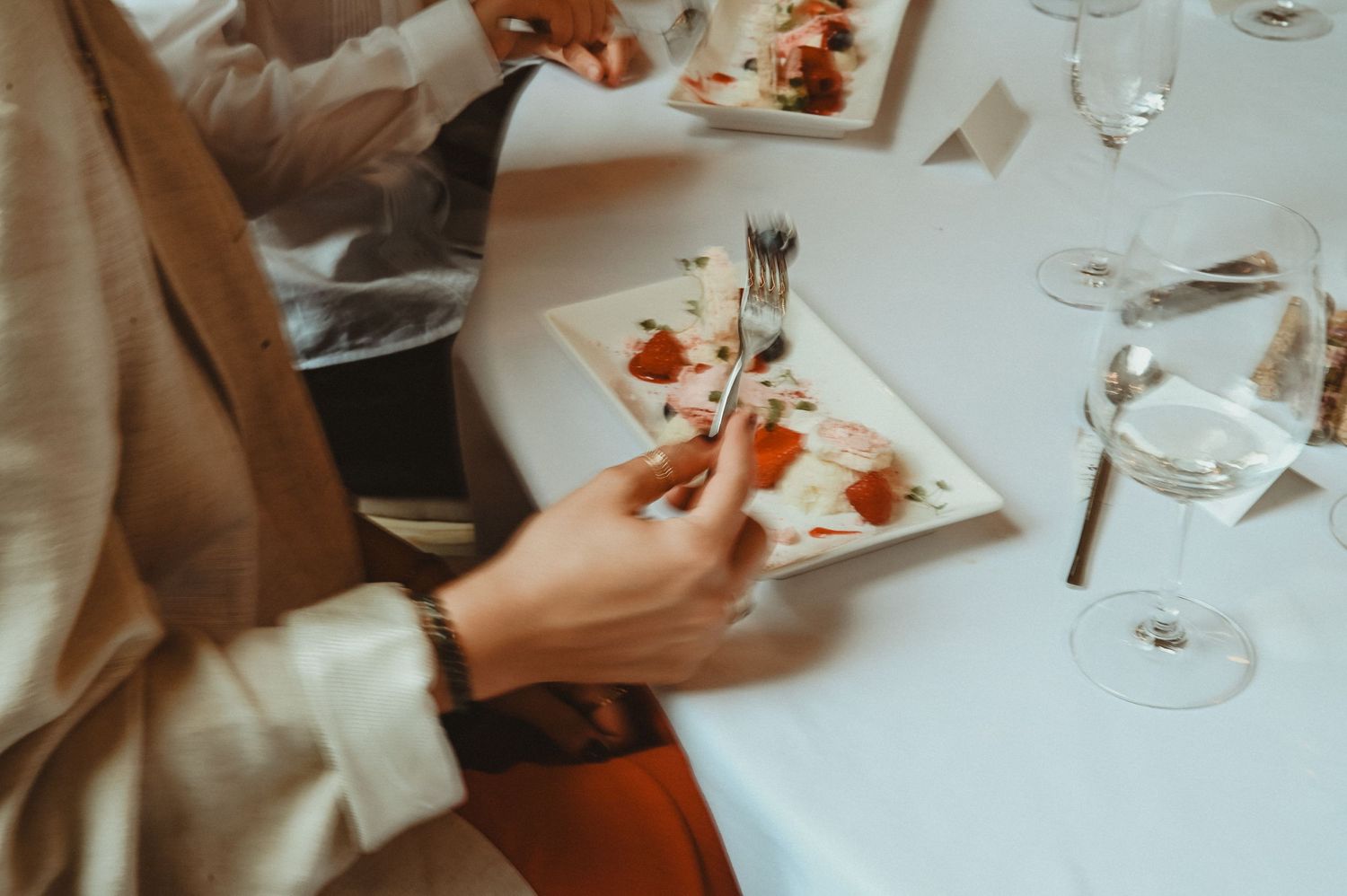 Close-up of hands with elegant place settings and appetizers at formal dining event.