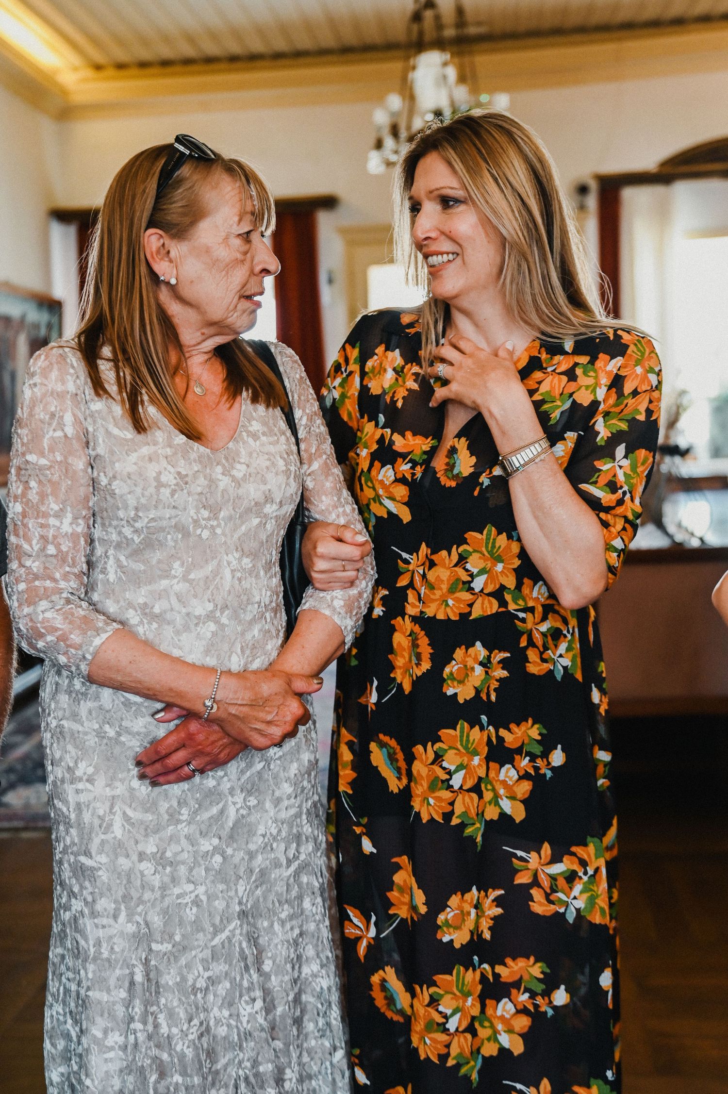 Two people share a conversation while wearing elegant dresses indoors.