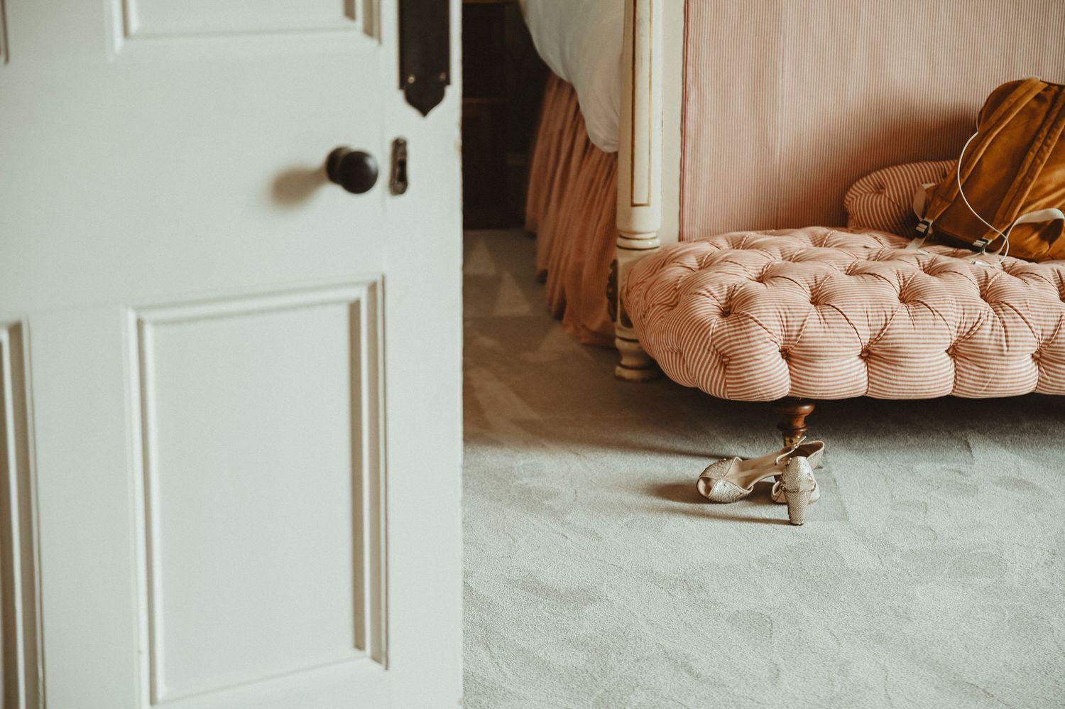 White door frame leading to room with pink tufted ottoman and vintage furnishings.