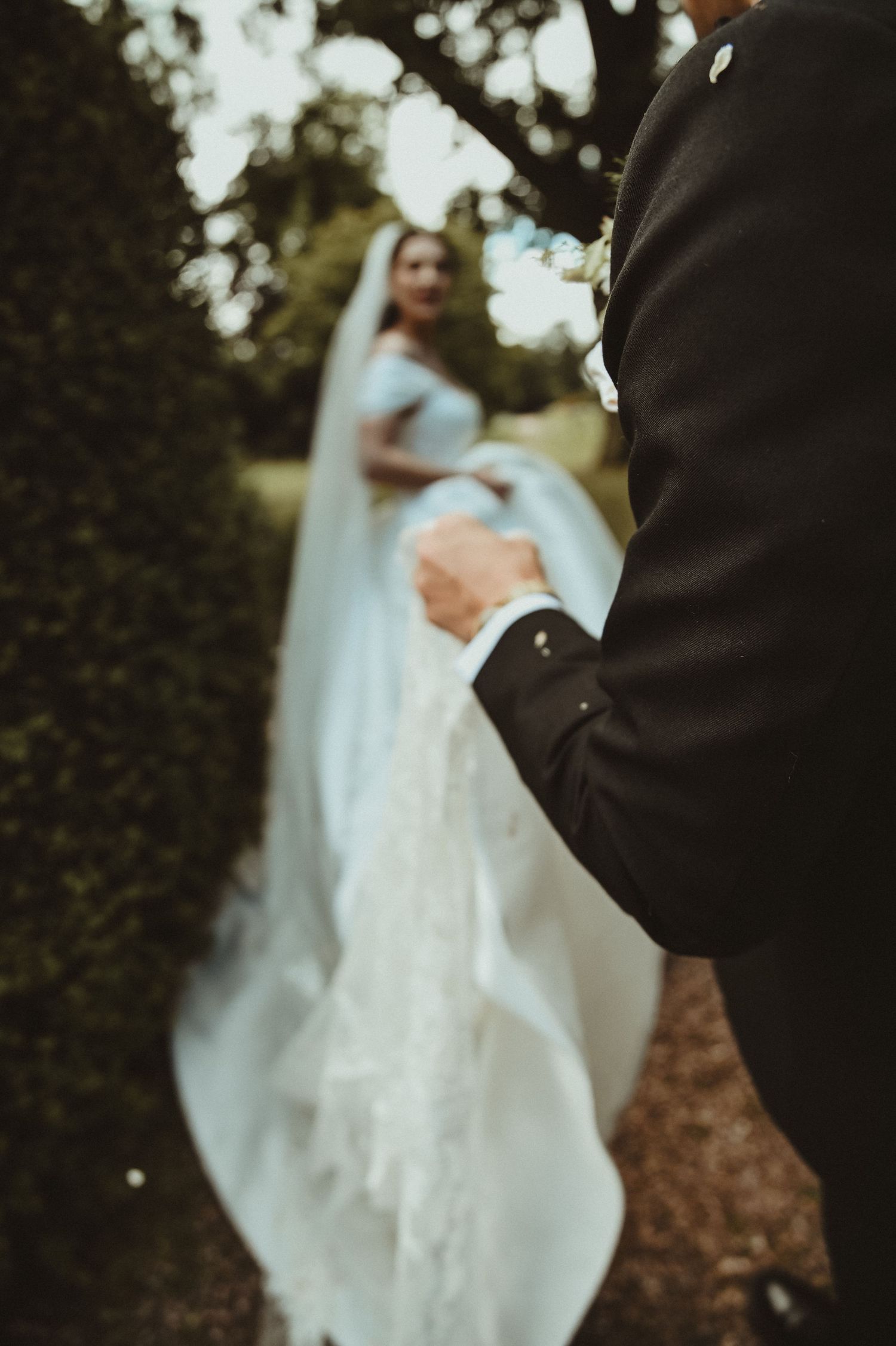 A close-up detail shot of a bride's white wedding dress and groom's suit.