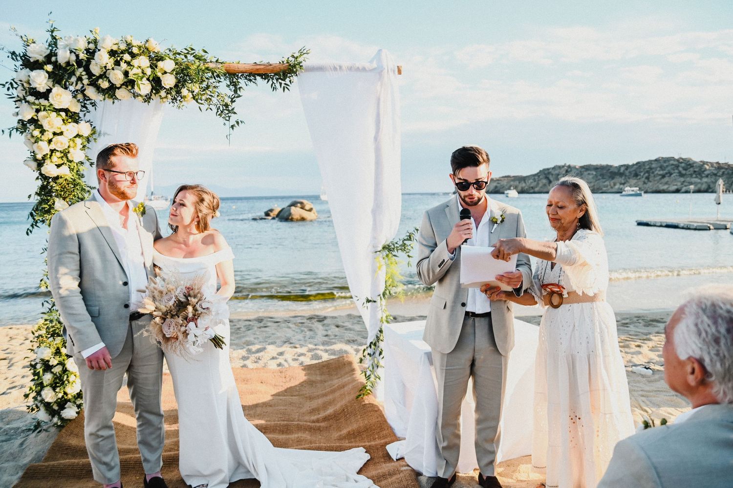 Wedding ceremony on a beach with elegant floral arch and white decorations by the sea.